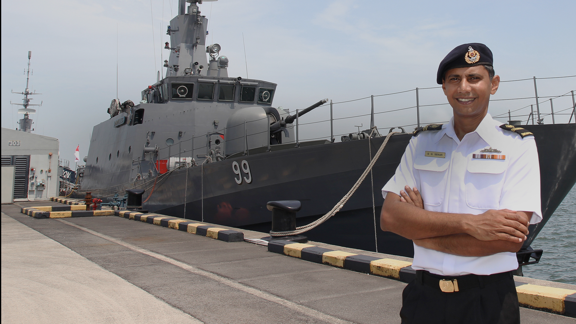 ME4 Ganasekar in beret poses proudly beside a docked patrol vessel.