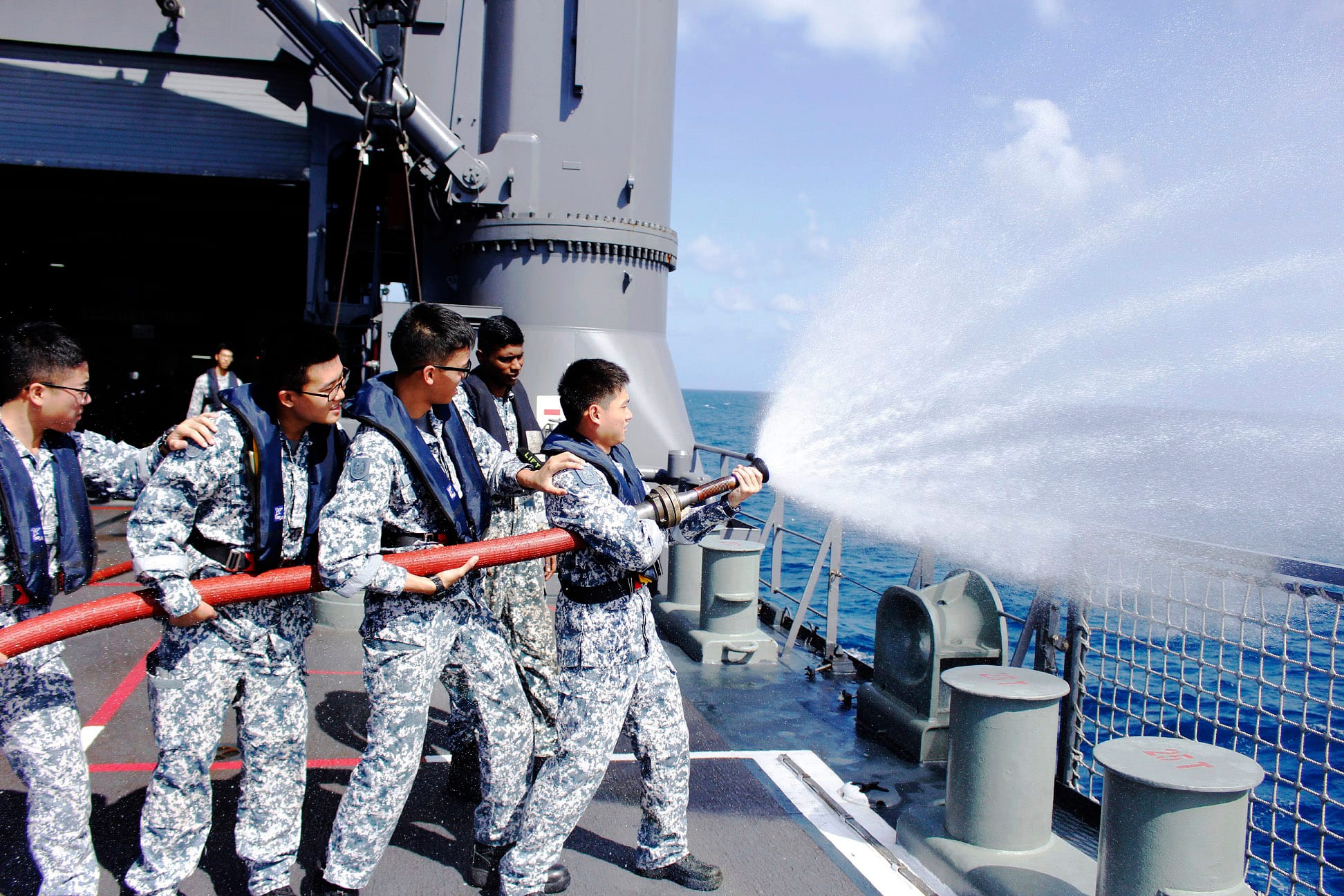 Sailors train on a ship’s deck by operating a water hose as part of a fire-fighting drill at sea.