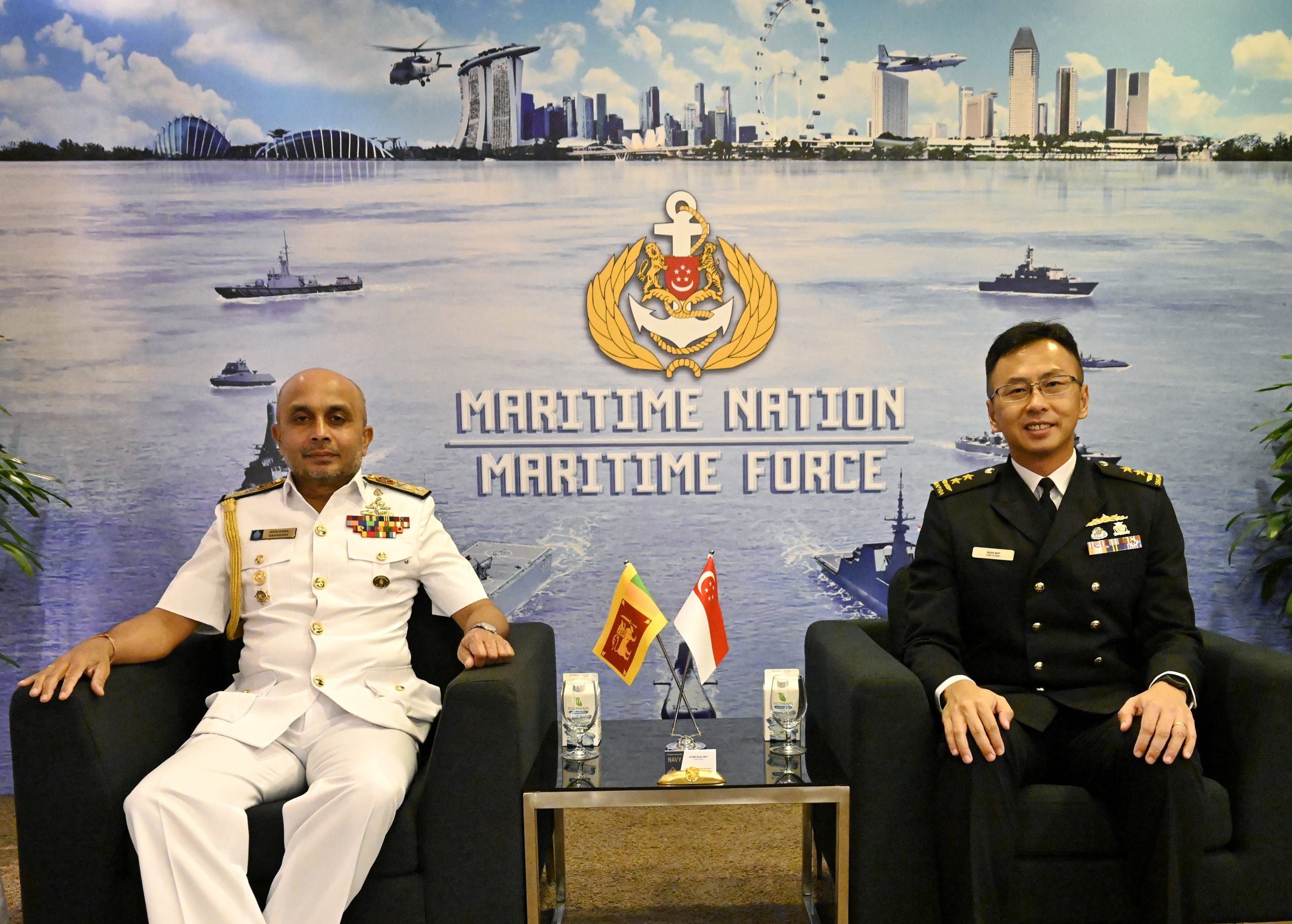 Two naval officers seated, with flags of Sri Lanka and Singapore in front, backdrop of Maritime Nation Maritime Force.