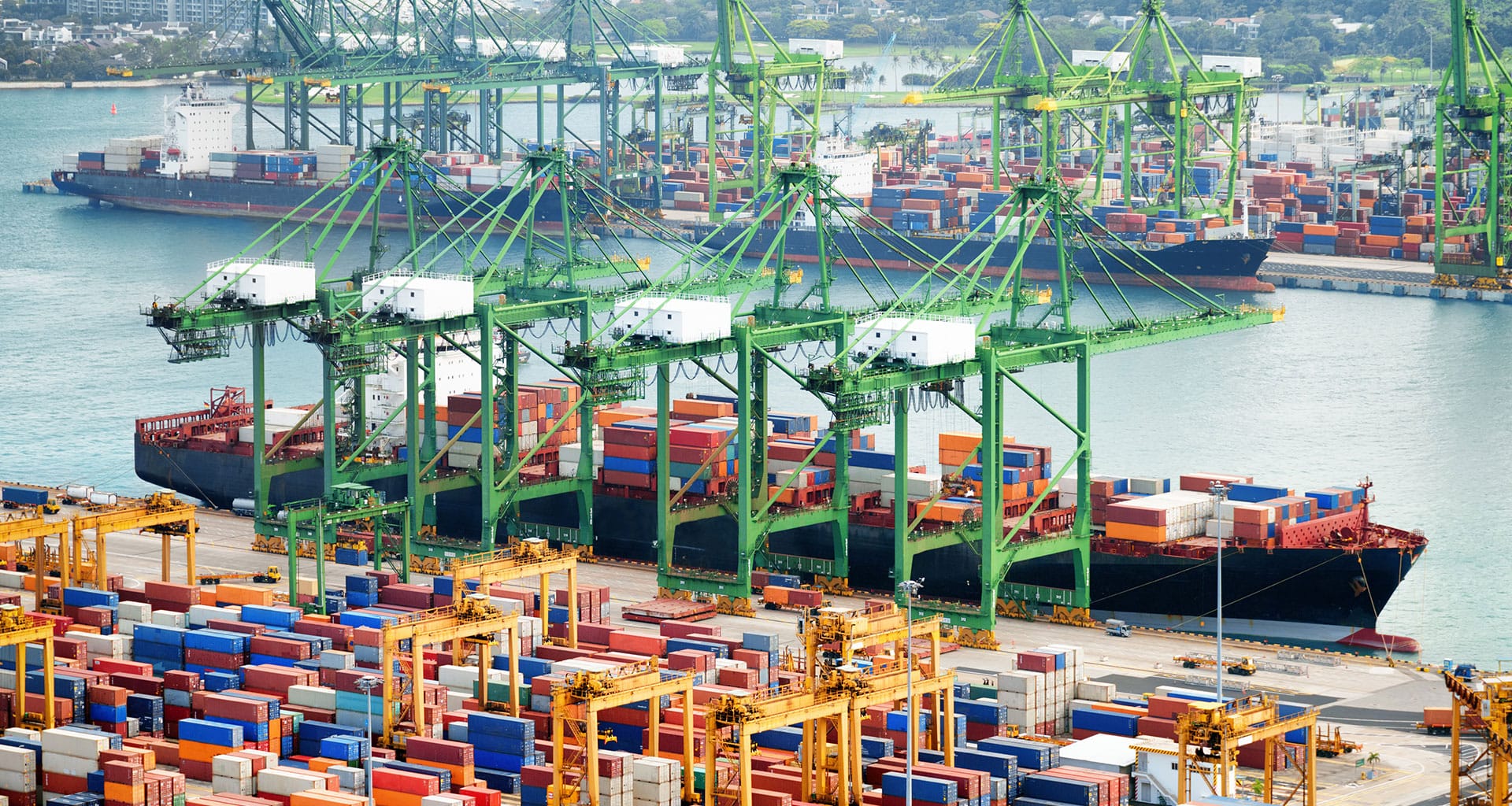 Aerial view of shipping containers and cranes at a bustling port terminal.