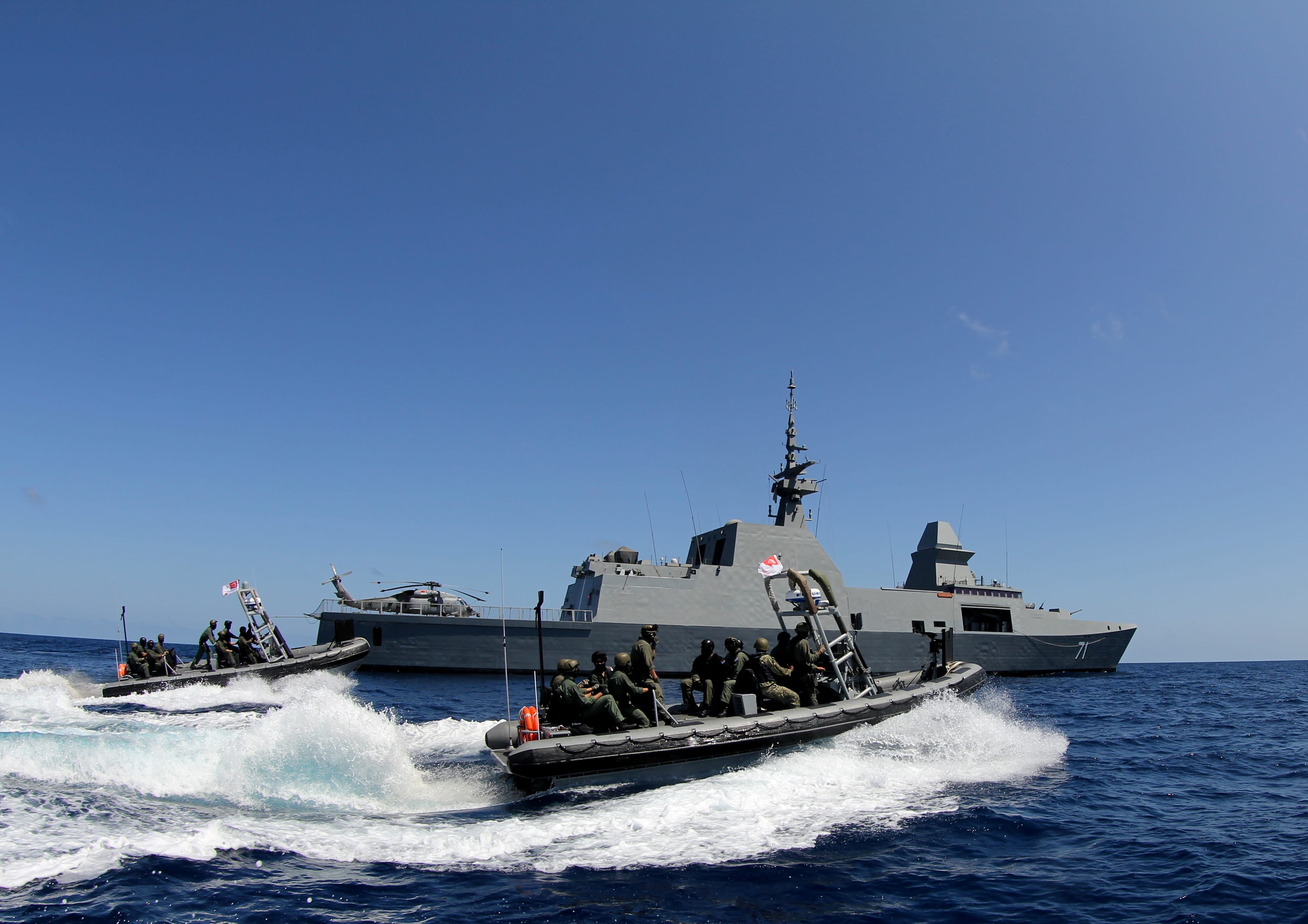 Singapore Navy personnel in fast boats maneuvering near a warship in the open sea.