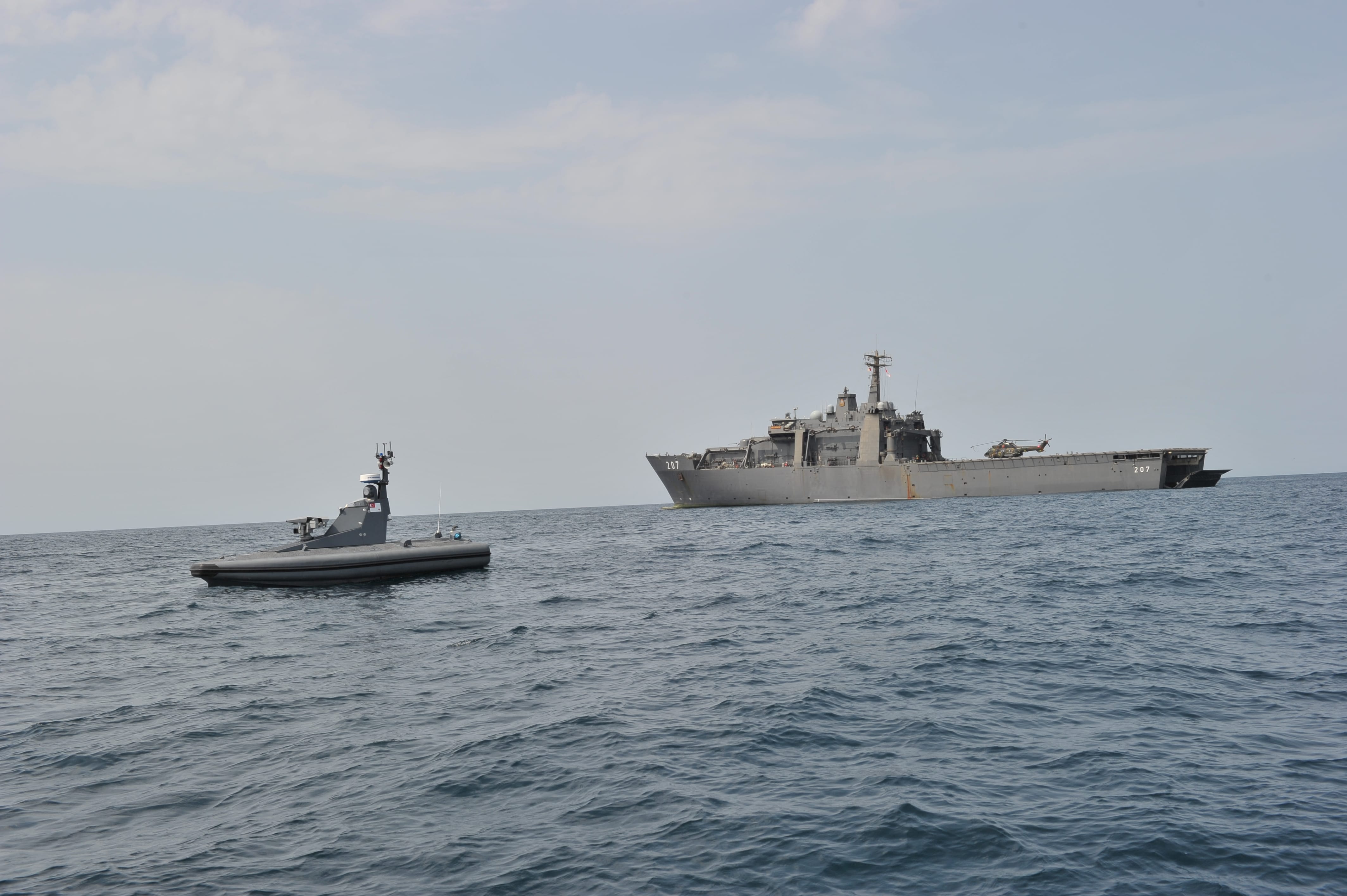 A military vessel and an unmanned surface vessel in the ocean.