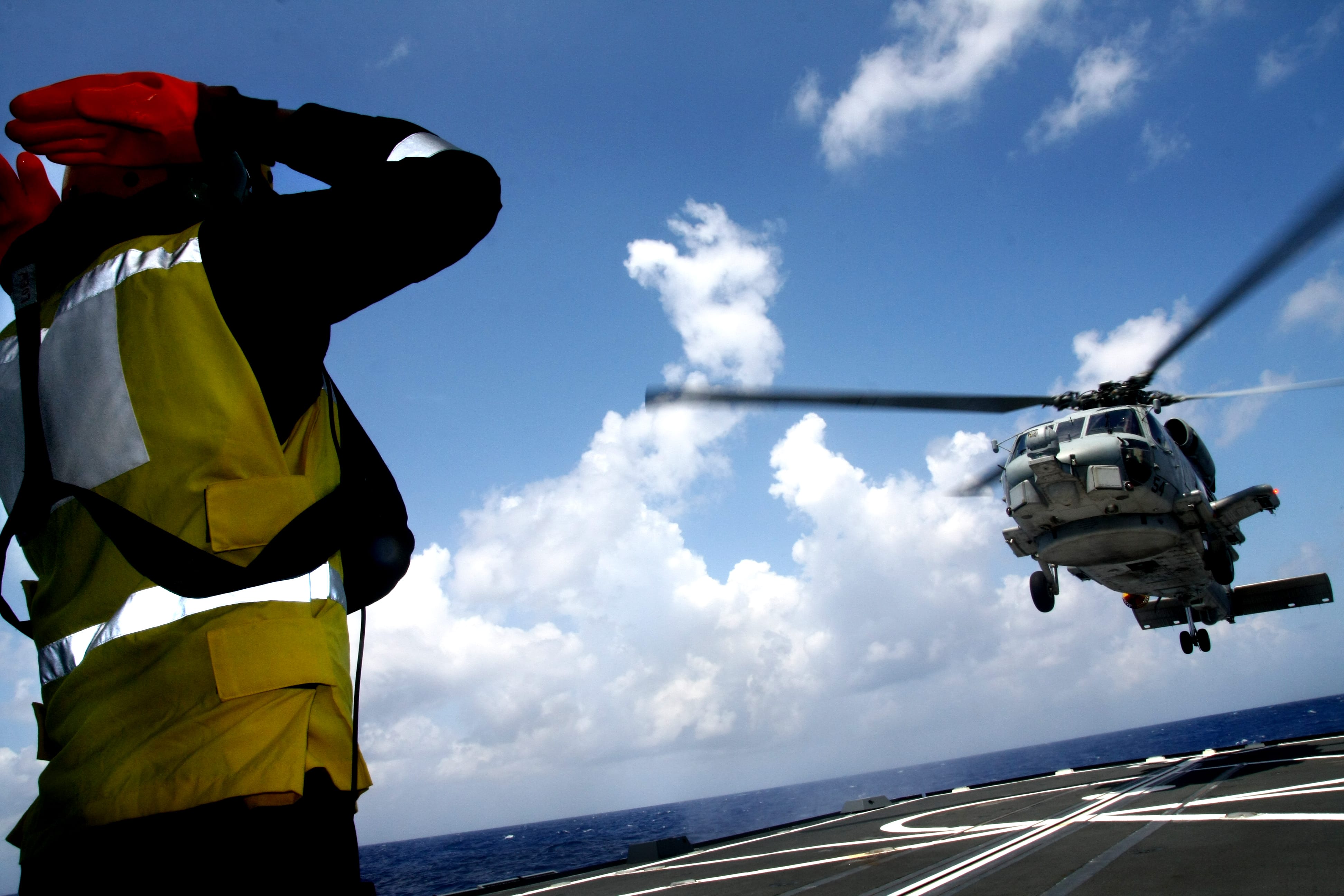 A Singapore Navy sailor salutes a helicopter during its takeoff on a ship's deck.