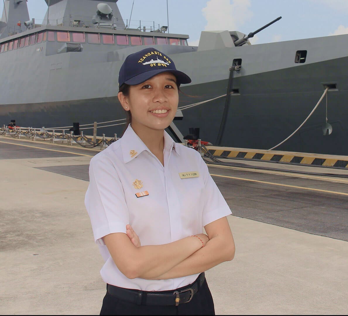 Naval officer Winnie Lai stands smiling on the pier beside a docked Republic of Singapore Navy warship.