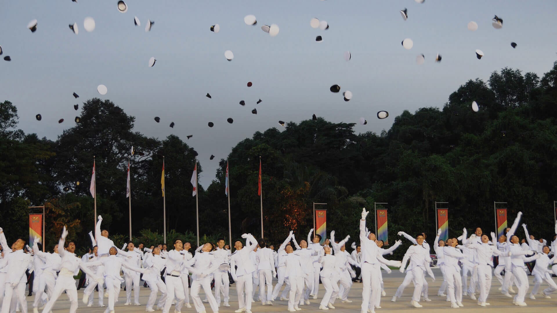 SAF officer cadets in white uniforms celebrate by tossing caps into the air during a graduation parade.
