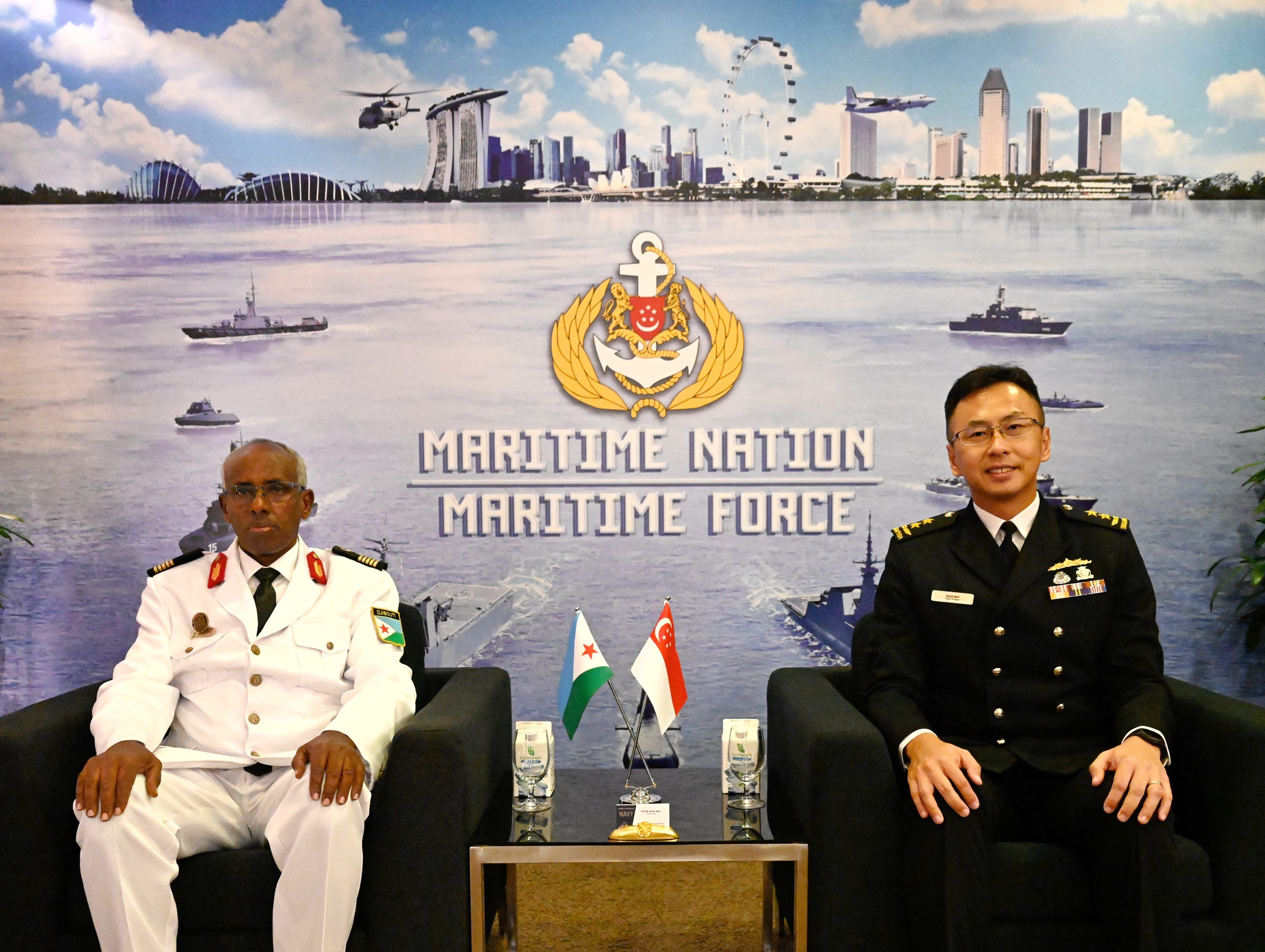 Two naval officers seated, with flags of Djibouti and Singapore in front, backdrop of Maritime Nation Maritime Force.