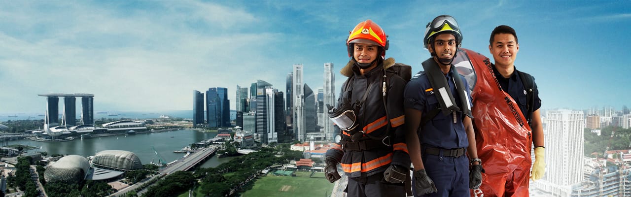 Three SCDF officers in different rescue gear posed with city skyline behind.