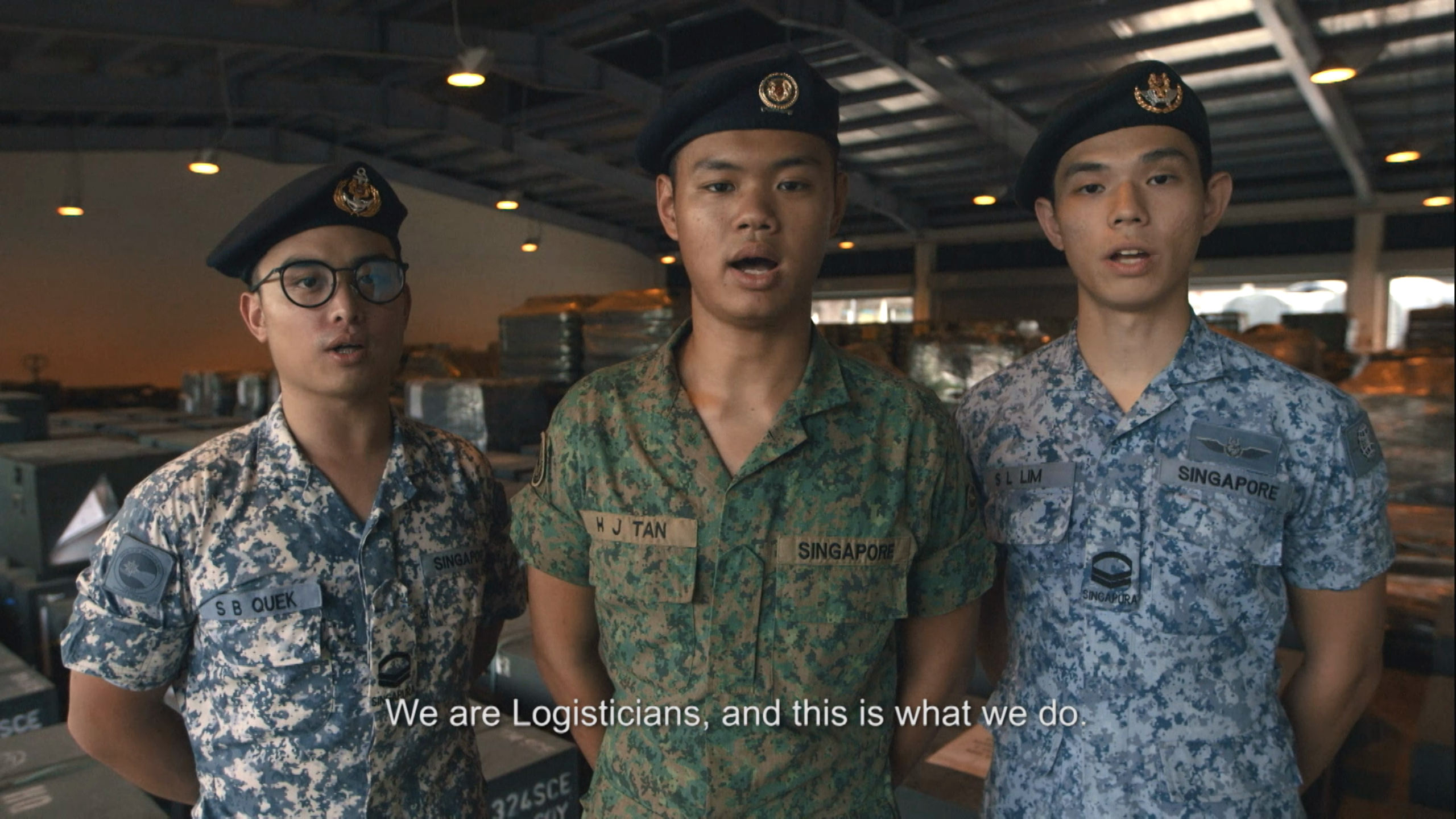 Three SAF logisticians from different services standing in front of supplies.