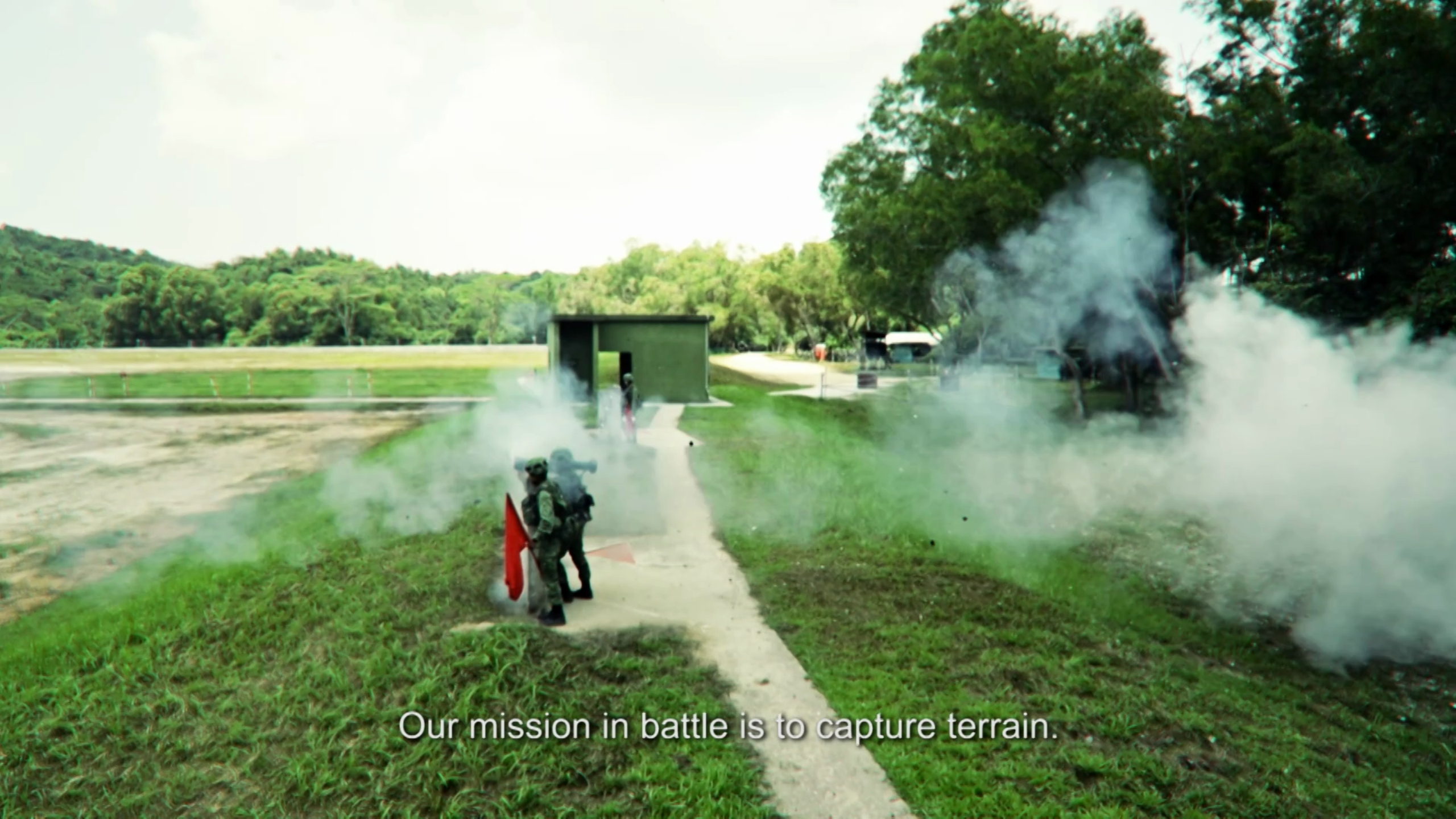 Infantry troops advancing through training grounds amid smoke grenades.
