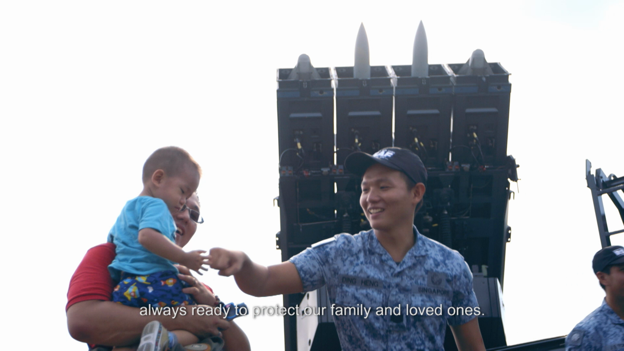 Air Force officer greets child during air defence display with missile system in background.