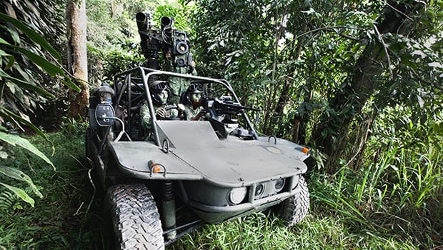 Guardsmen in light strike vehicle camouflaged in dense jungle environment.