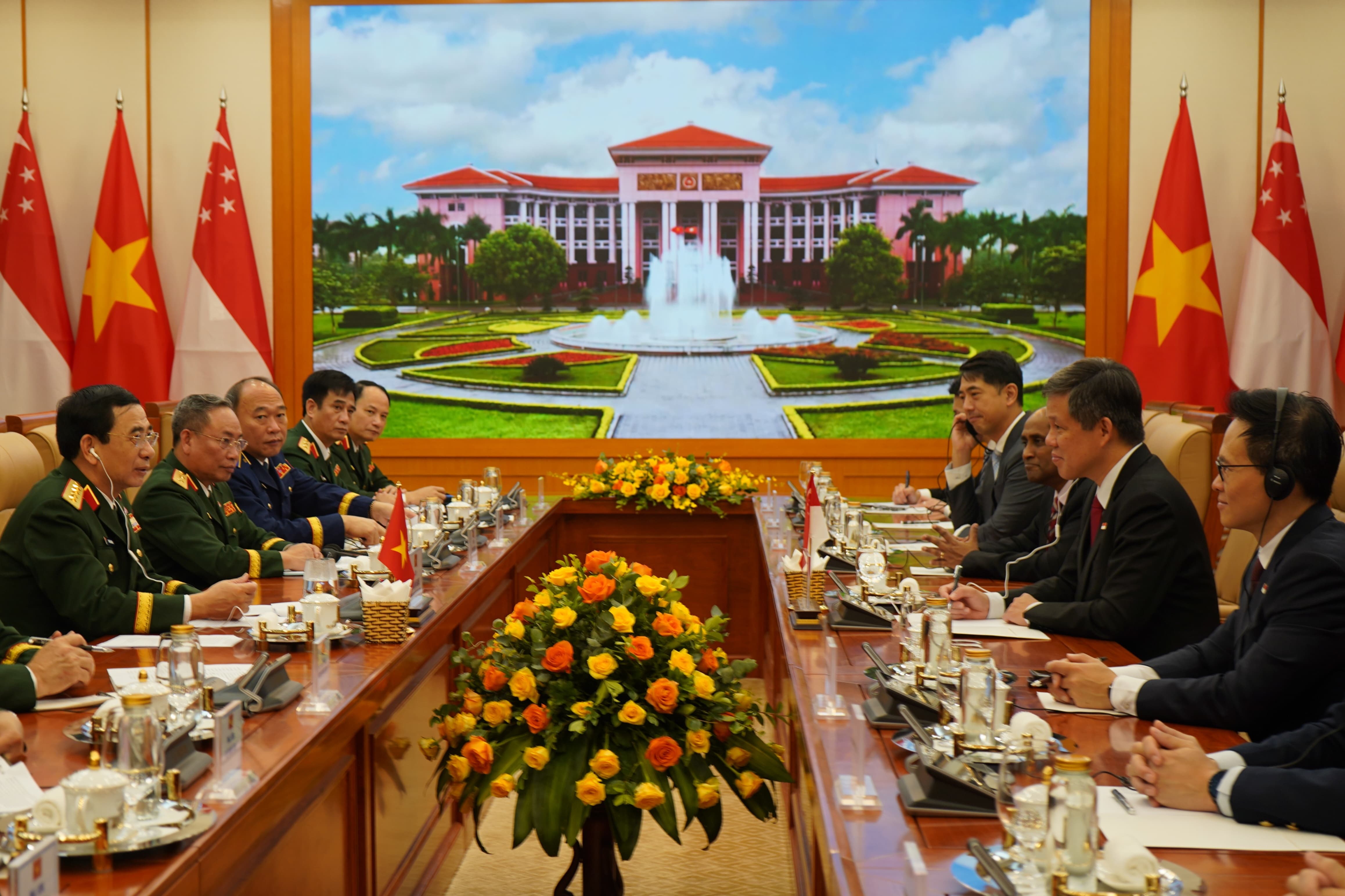 Meeting with Vietnamese and Singaporean flags, floral arrangements, building image in background.