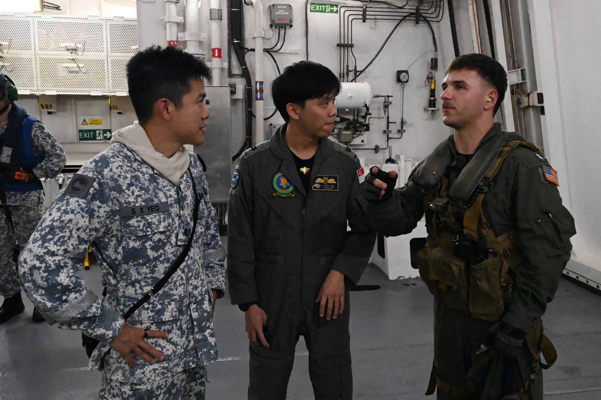 A RSN serviceman and an RSAF S-70B Seahawk crew member interacting with a United States Navy (USN) counterpart after the successful cross-deck landing of a USN MH-60R helicopter on RSS Supreme.