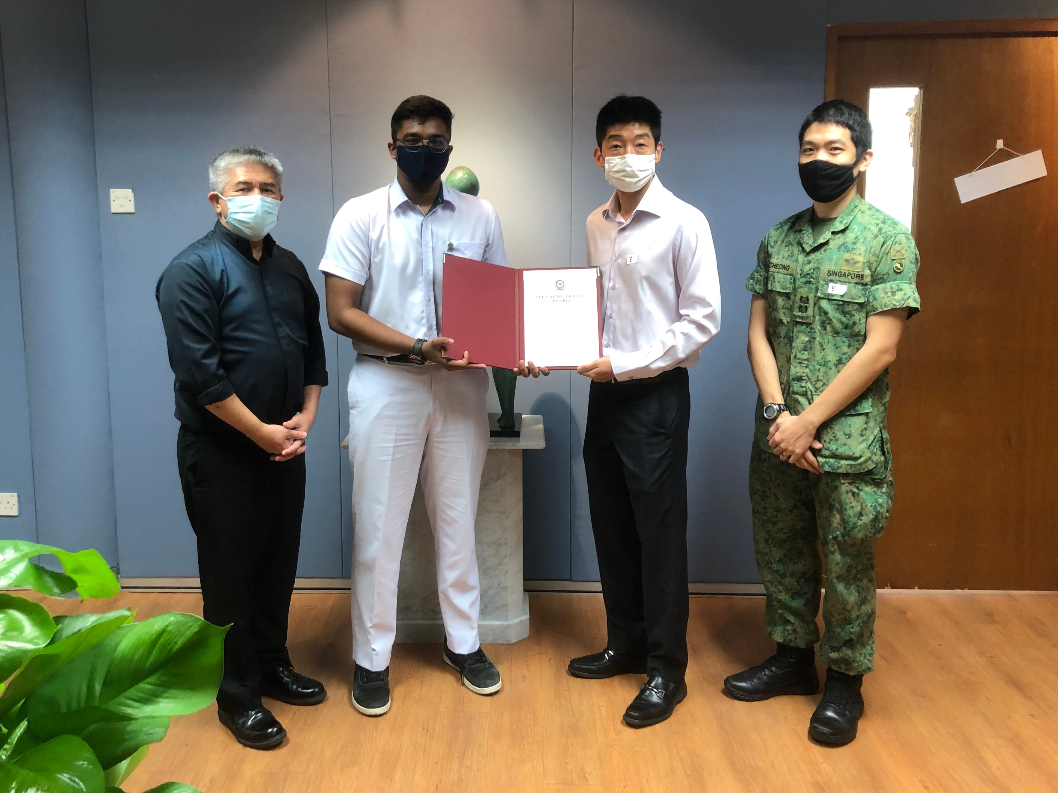 One student holding red folder stand with three adults, one in military uniform