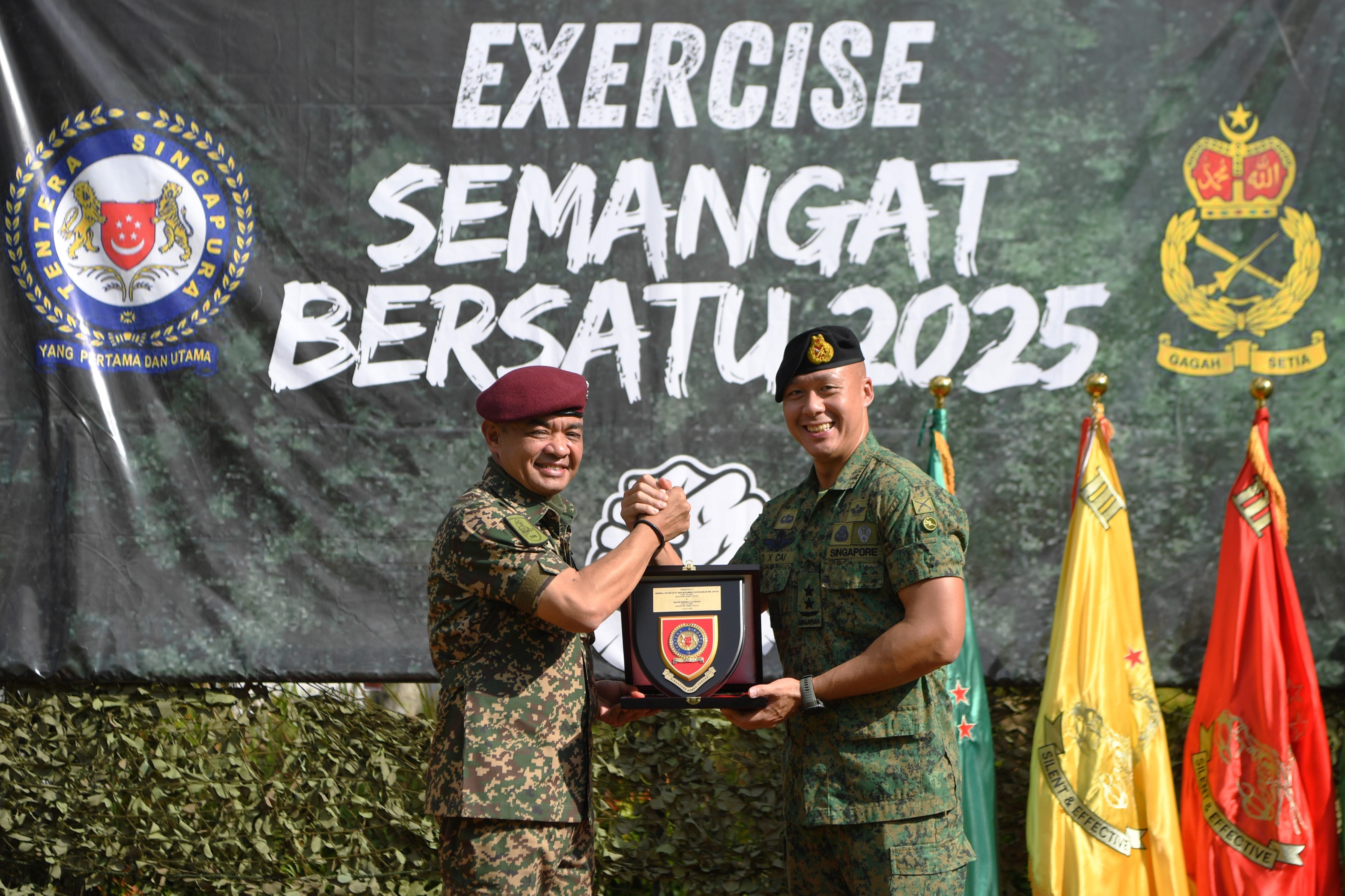 Two uniformed Singaporean soldiers exchanging an award in front of "Exercise Semangat Bersatu 2025" banner.
