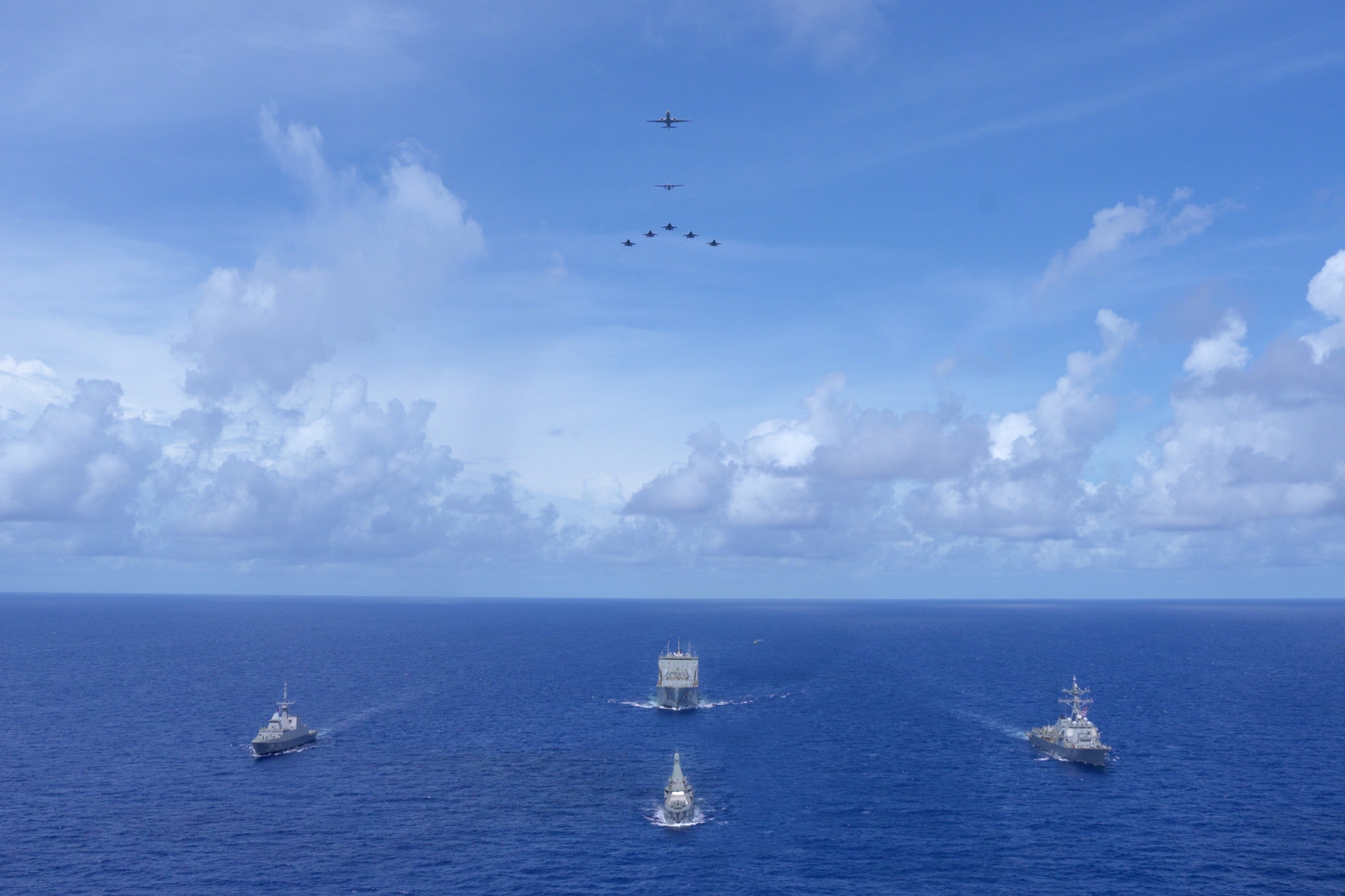 Exercise Pacific Griffin 2025 (XPG 25) ships, comprising (left) RSS Supreme, (top centre) USNS Charles Drew, (bottom centre) RSS Sovereignty, and (right) USS William P. Lawrence sailing in formation with participating aircraft flying overhead.