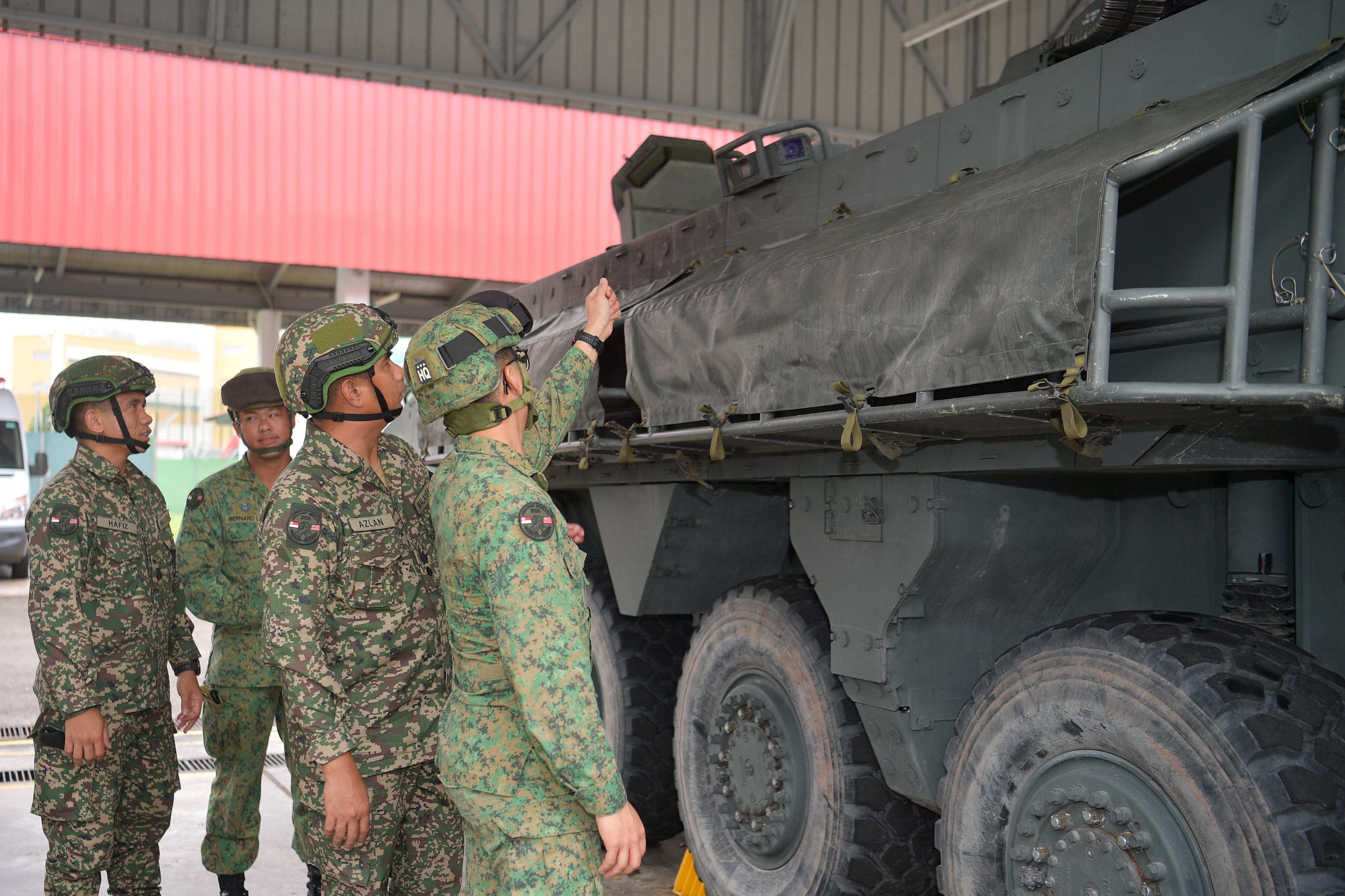 Soldiers in camouflage uniforms inspect a large military vehicle with covered cargo.