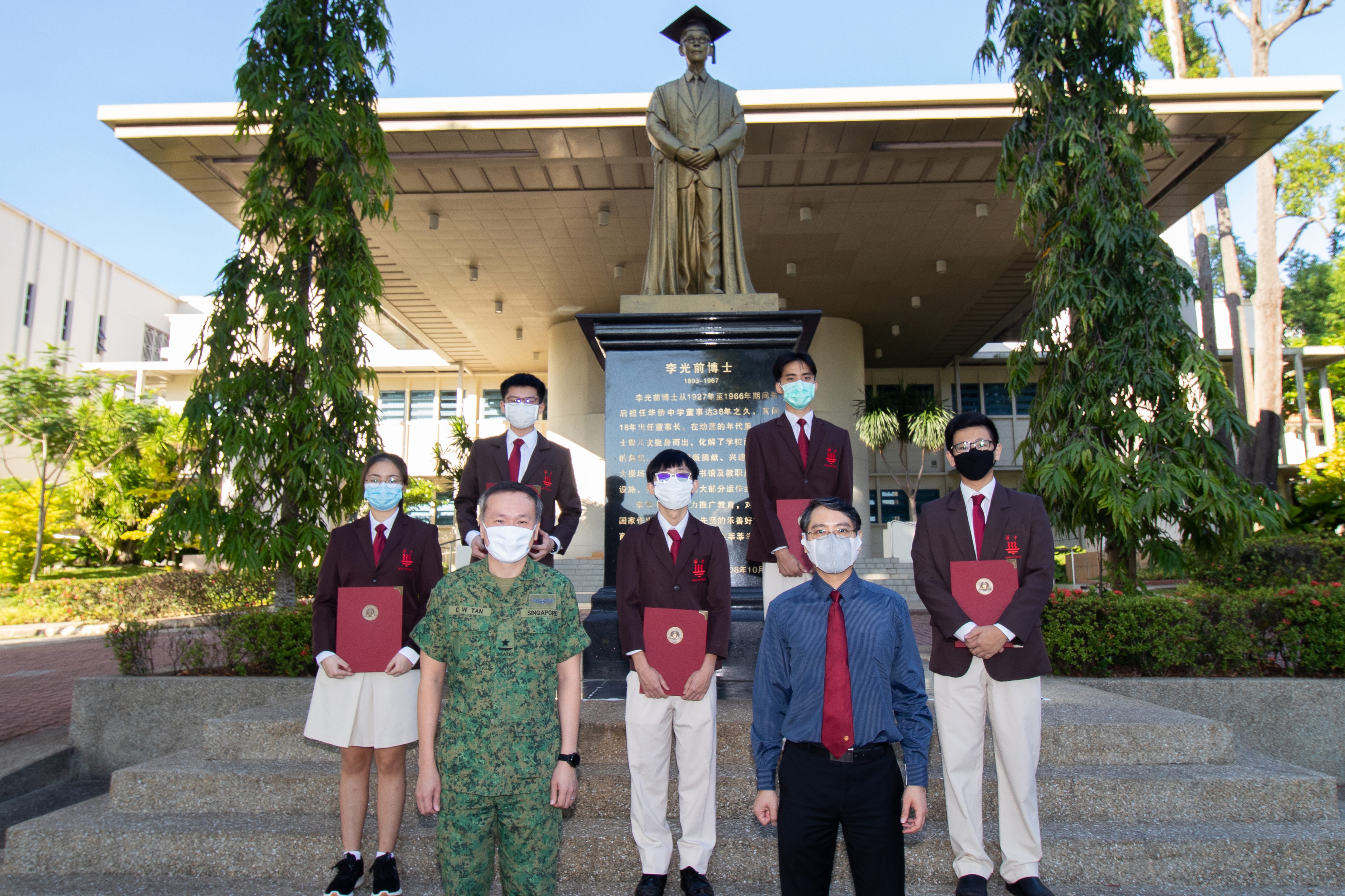Five students holding red folders stand with two adults, one in military uniform
