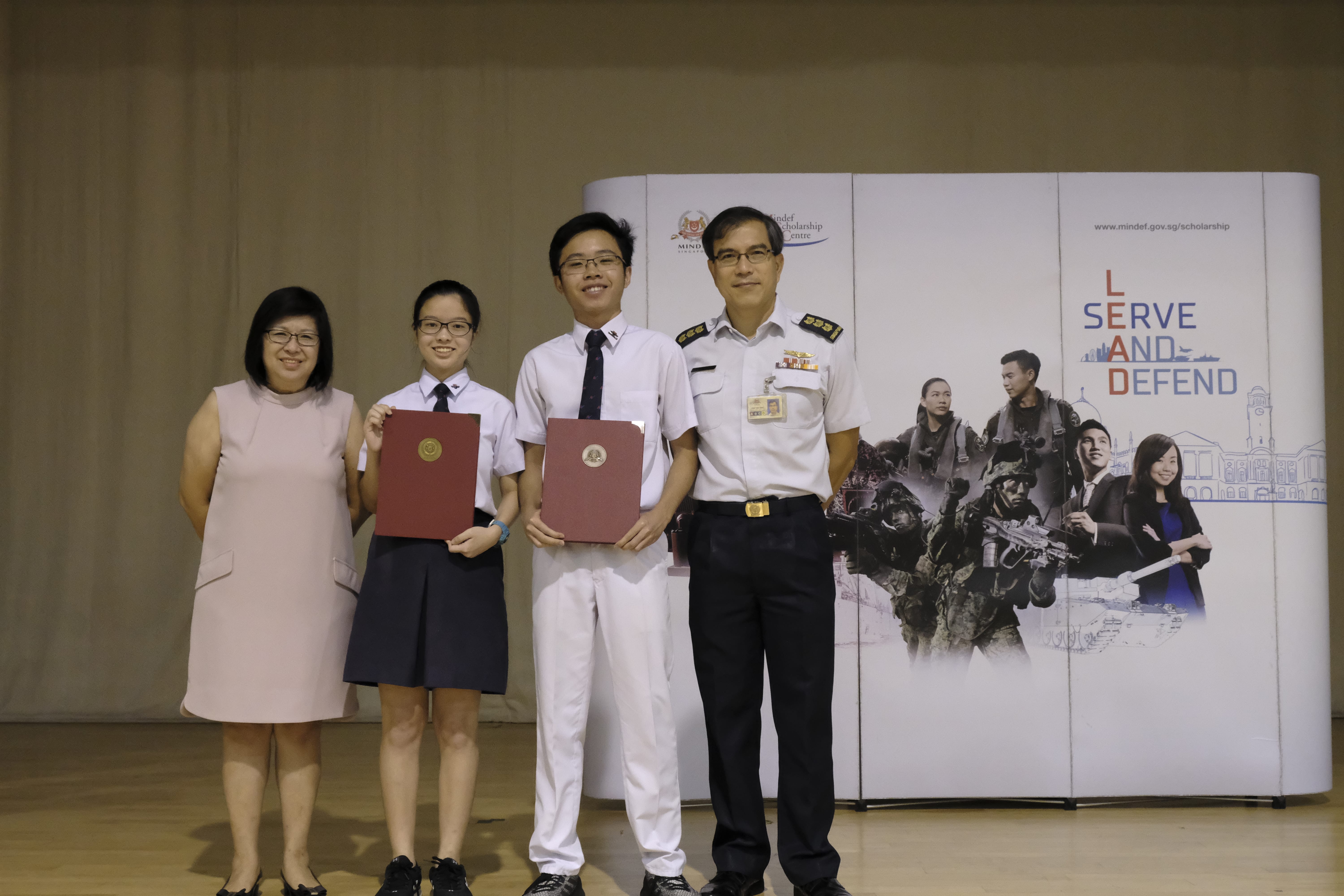 Two students holding red folders stand with two adults, one in military uniform