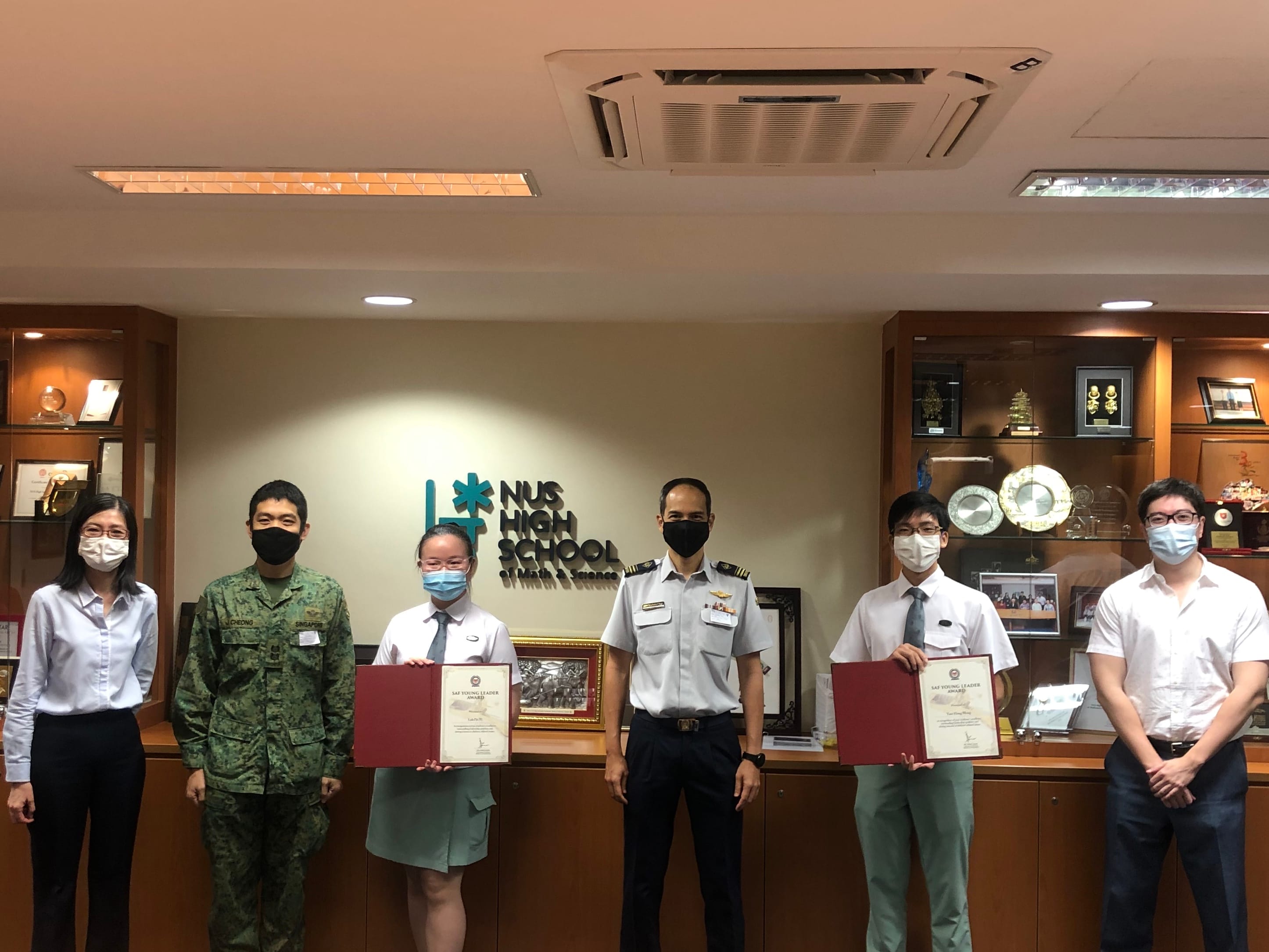 Two students holding red folders stand with three adults, two in military uniforms