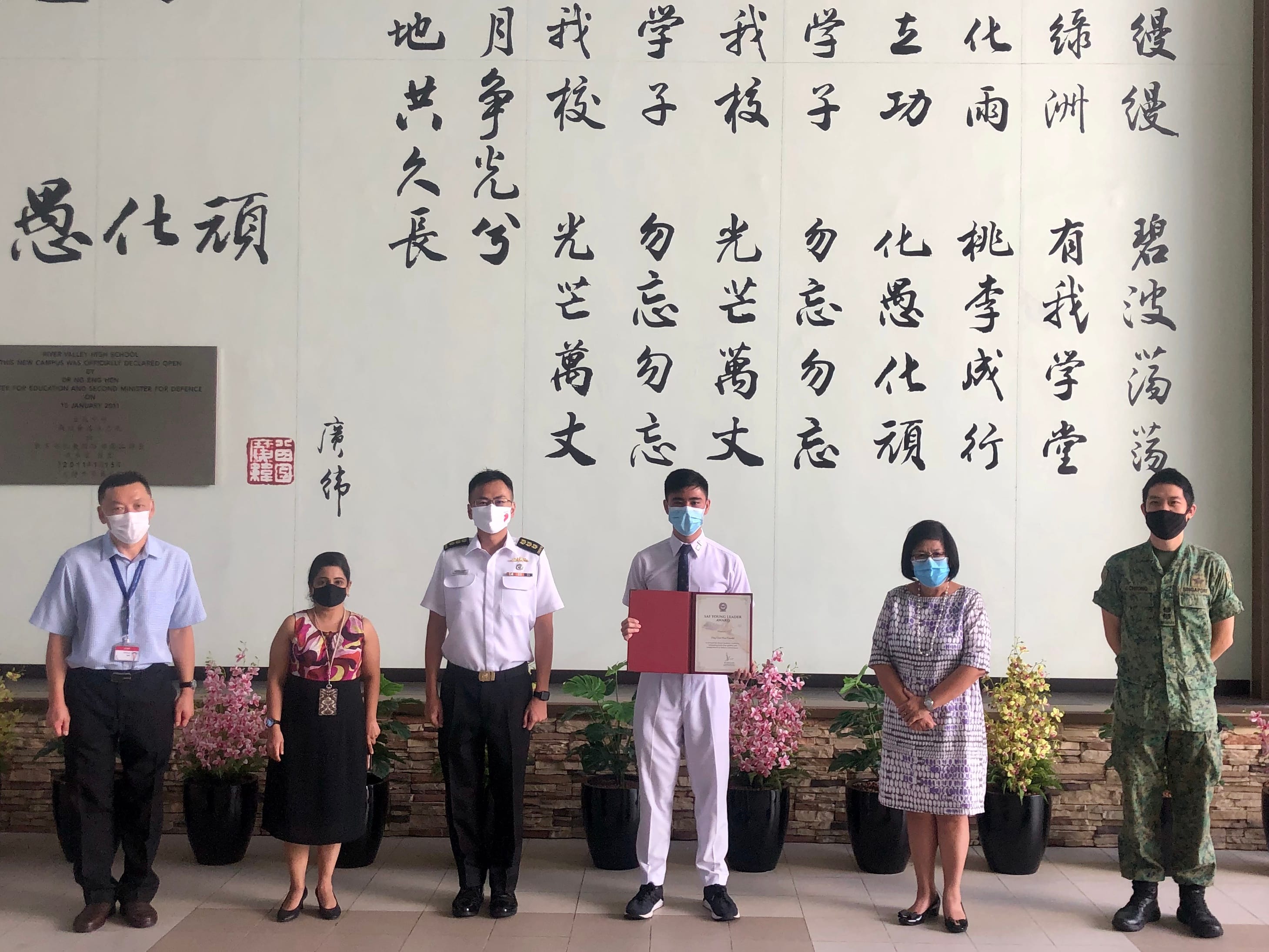 One student holding red folder stand with five adults, two in military uniforms