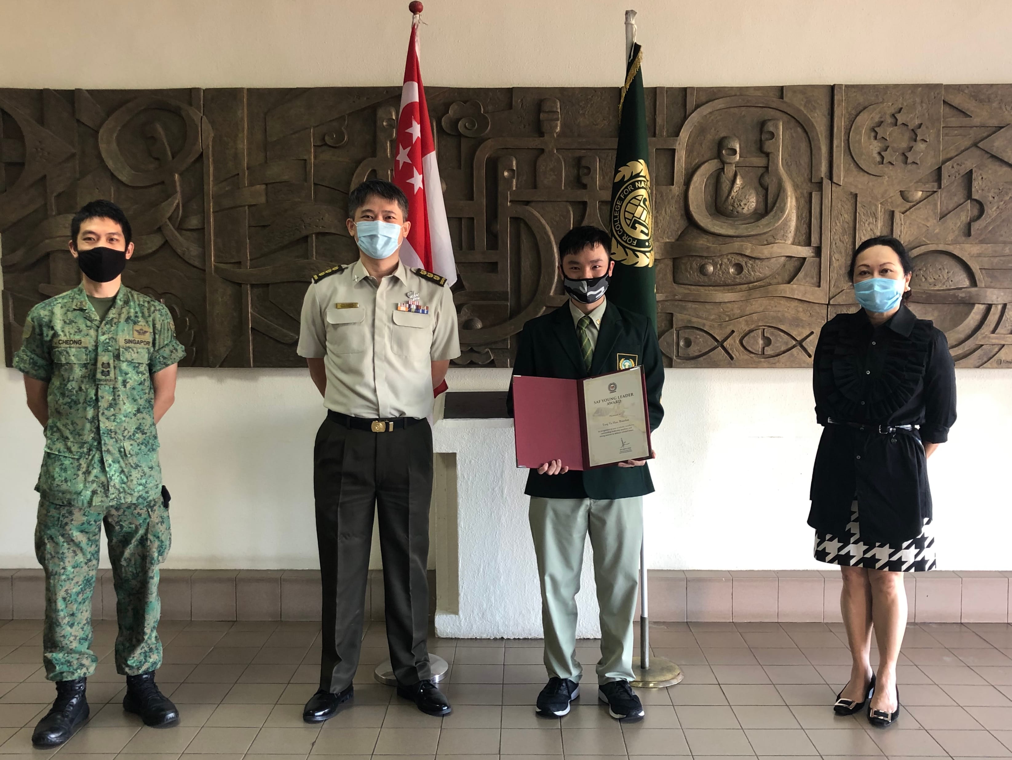 One student holding red folder stand with three adults, one in military uniform