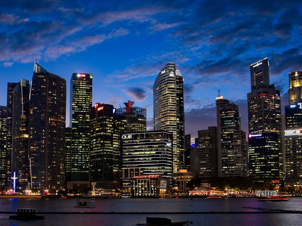 Night cityscape featuring skyscrapers, water, and branded signs for UBS and HSBC.