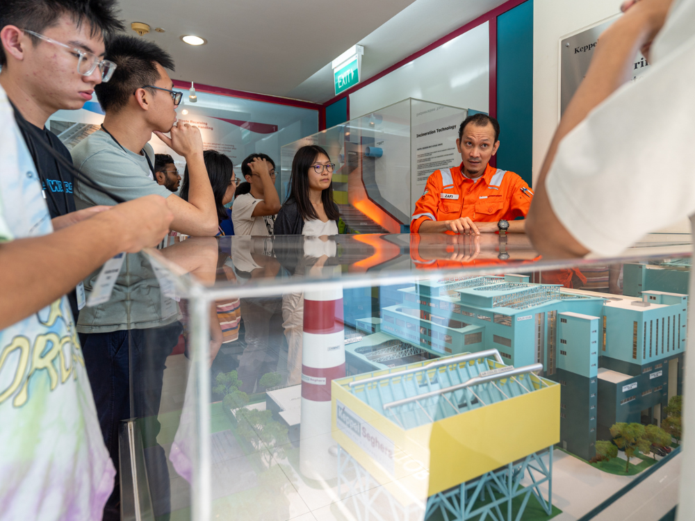 Group viewing architectural model under glass; man in orange uniform.