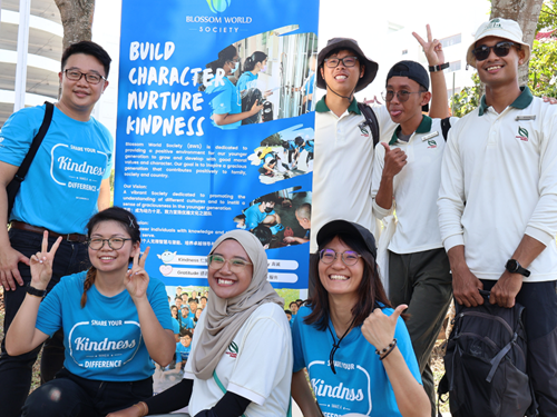 Volunteers in blue and white shirts posing by a Blossom World Society kindness banner.