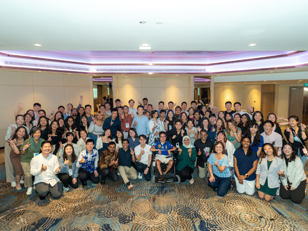 Large group of diverse people posing for a photo in a room with neutral walls.