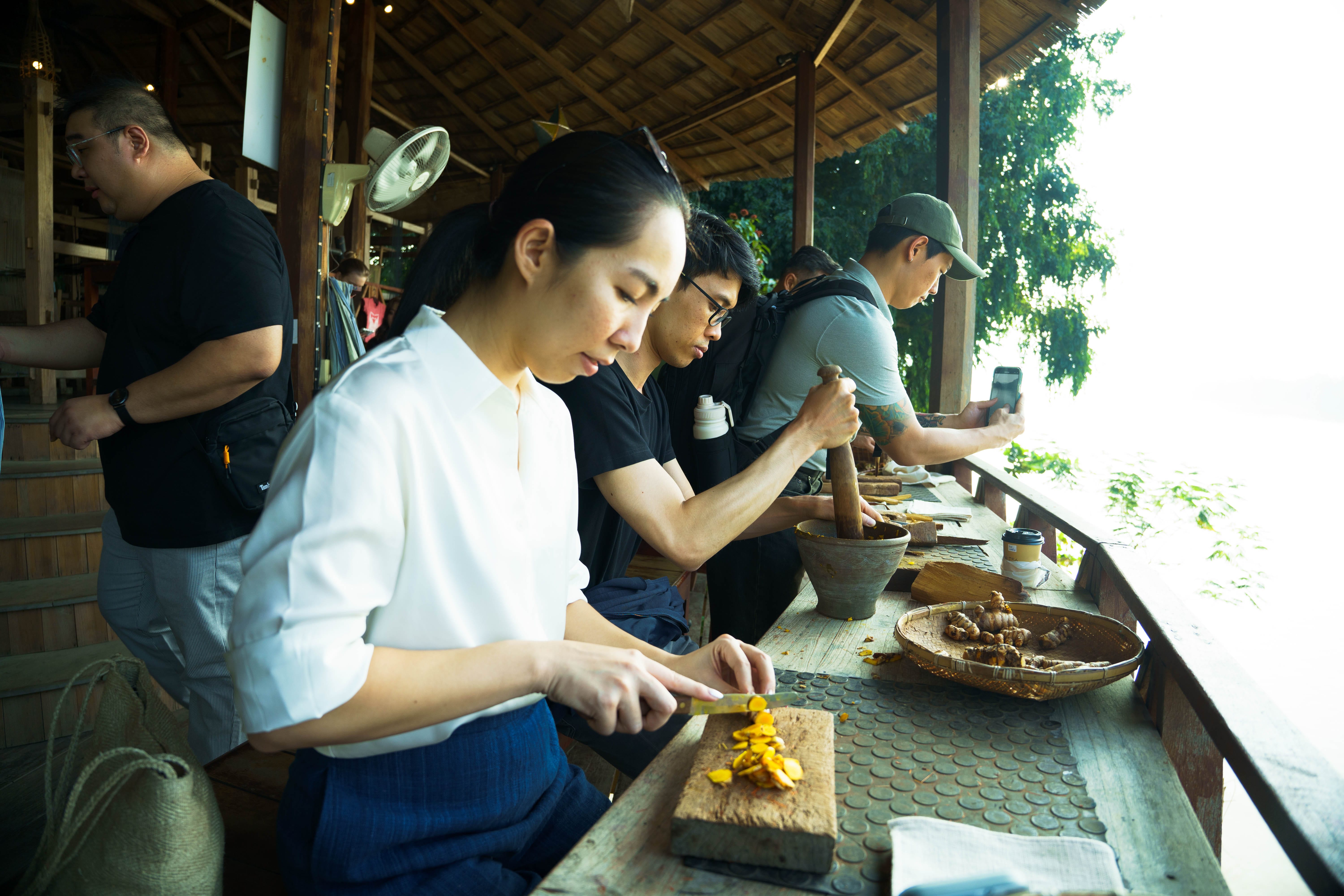 A few participants carrying out cooking activities, such as slicing, grinding. A participants take photos in the background.