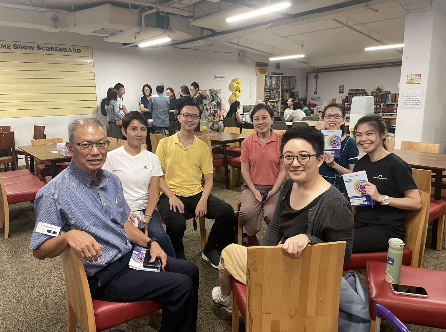 Group of diverse people seated in a room with tables and chairs.