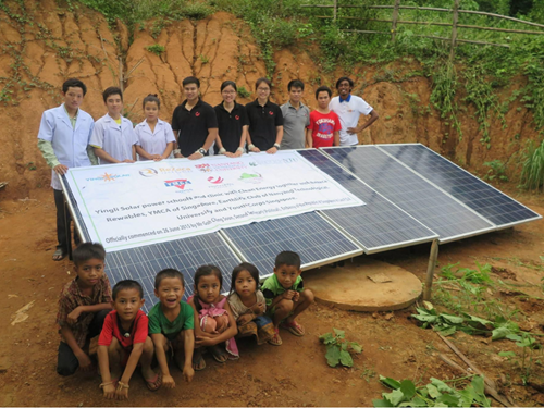 Youths and locals posing behind a solar panel installation project in a rural village