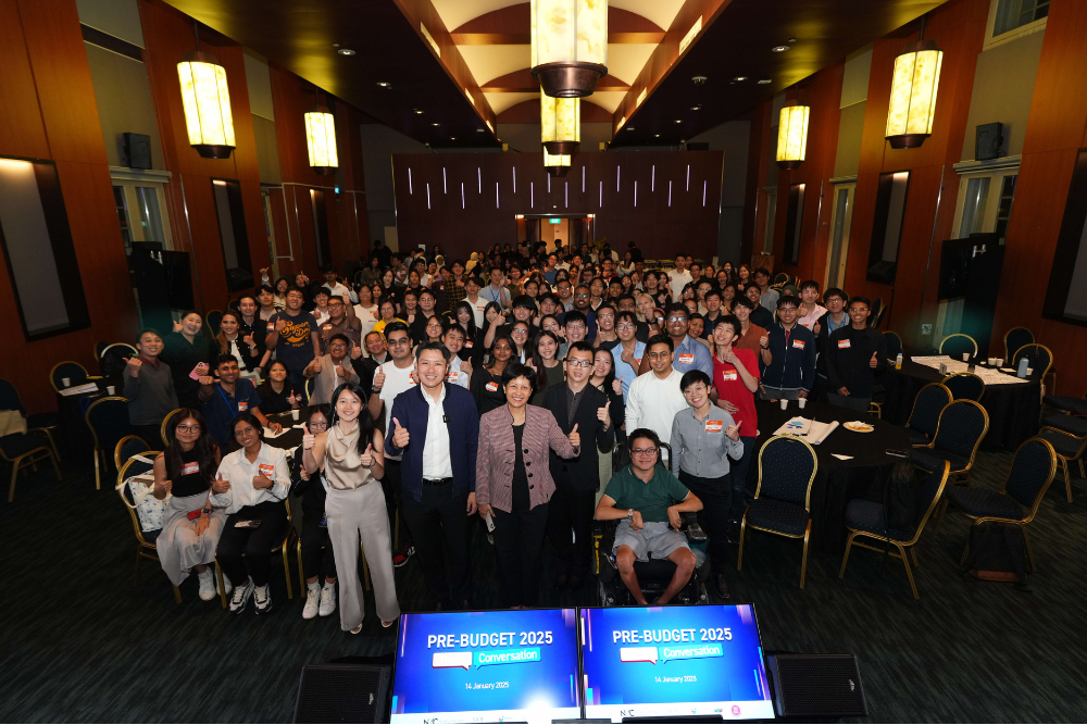 Large group of people giving thumbs up in a conference room, monitors read "Pre-Budget 2025".