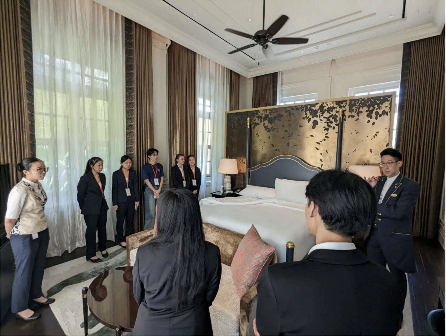 Group touring luxury hotel room, led by a staff member in uniform.