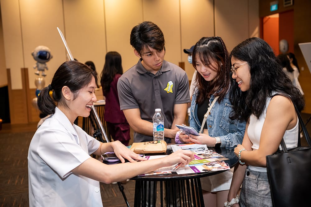 Students at table in event space, looking at brochures. An astronaut balloon figure is in the background.