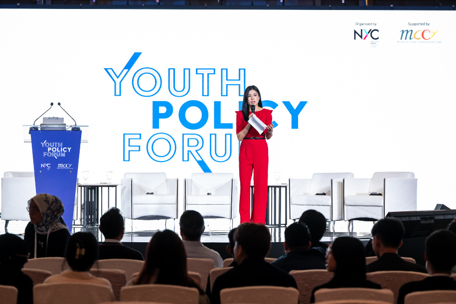 A lady in red on stage hosting the Youth Policy Forum.