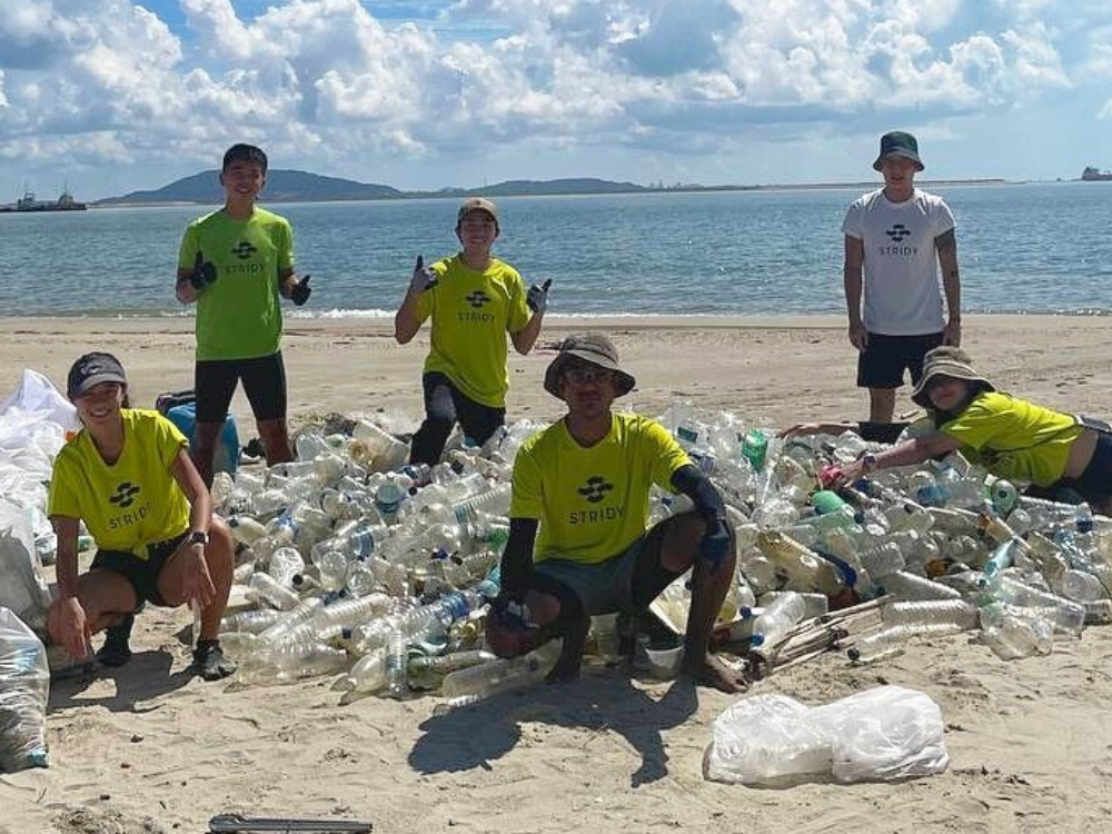 Volunteers on a beach pose with a large pile of collected plastic bottles and containers