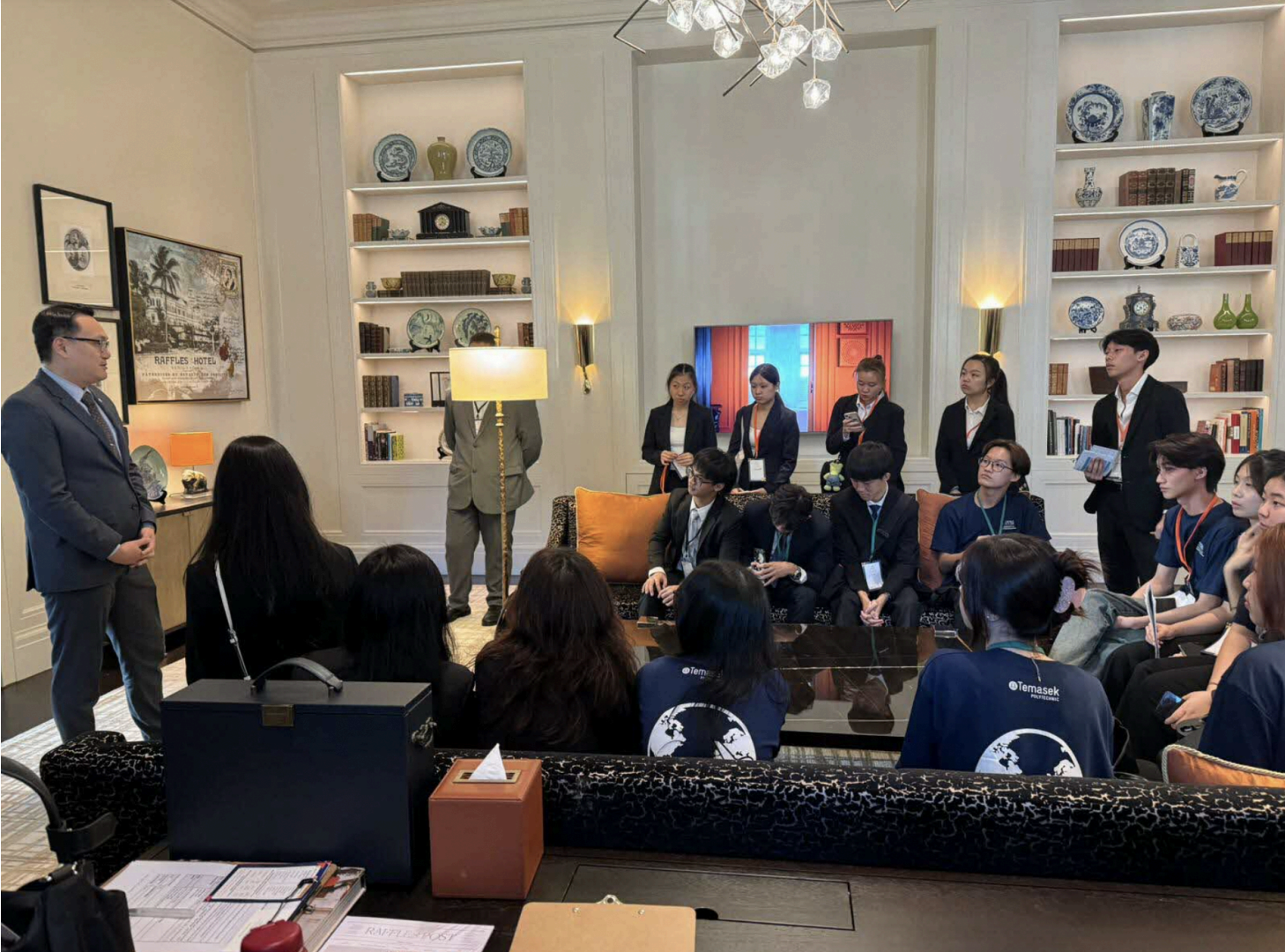 Group gathered in Raffles Hotel room listening to a speaker