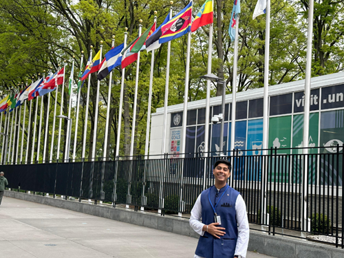 Dev Bahl posing outside the UN building, standing in front of a row of international flags