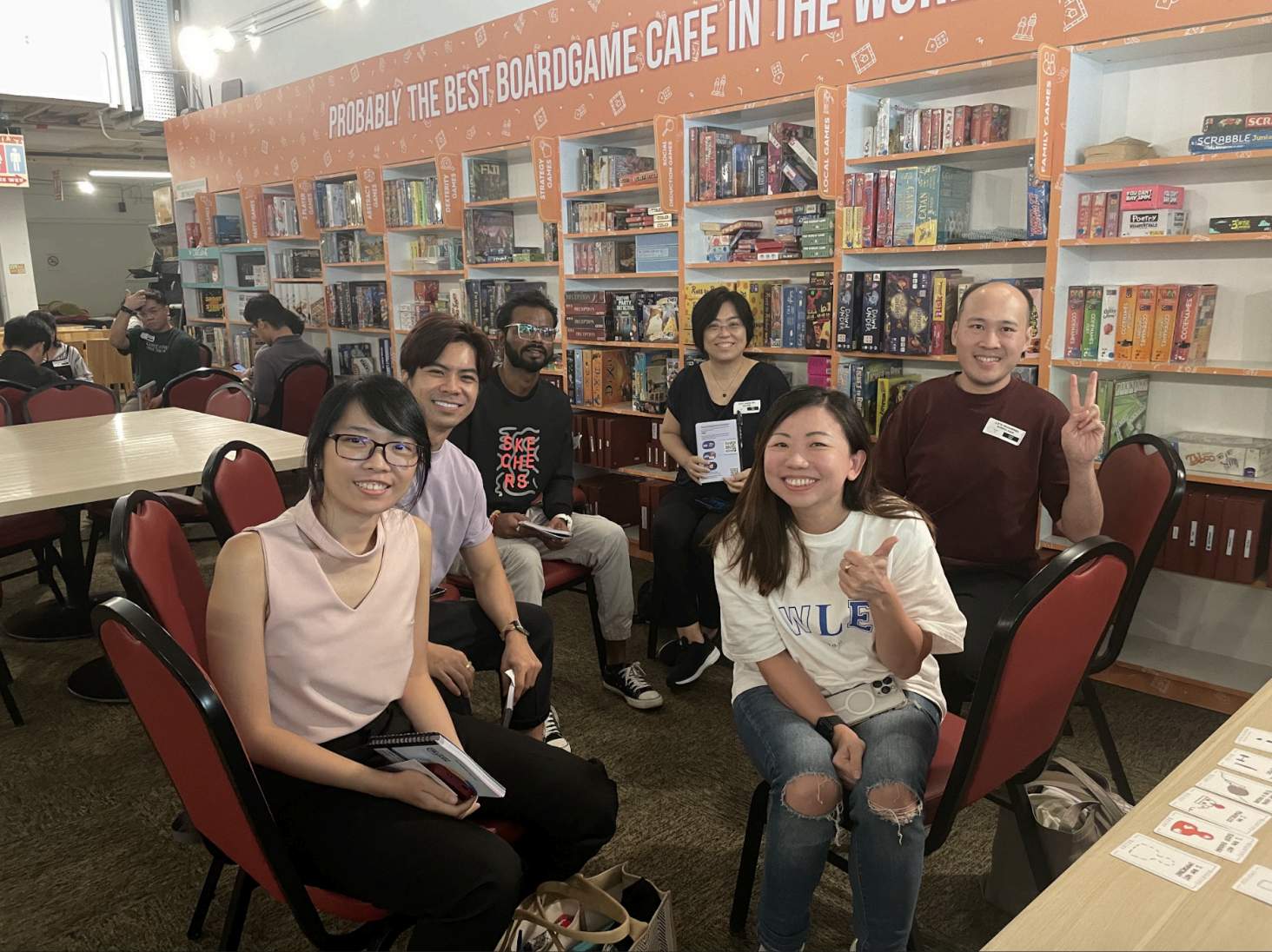 Group of people at boardgame cafe with shelves of board games.