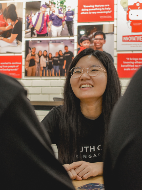 Anita smiling during a conversation, seated near a wall with posters on volunteerism