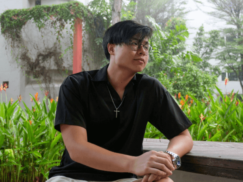 Jonasta in black shirt seated on bench outdoors, surrounded by greenery after the rain.