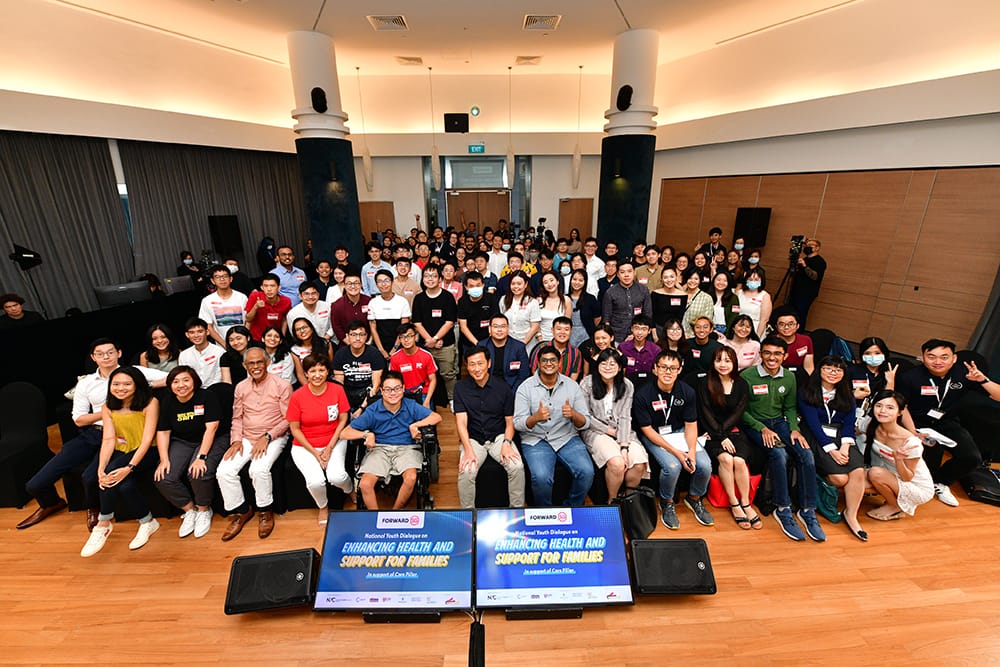Large group posed indoors with "Forward SG" banners