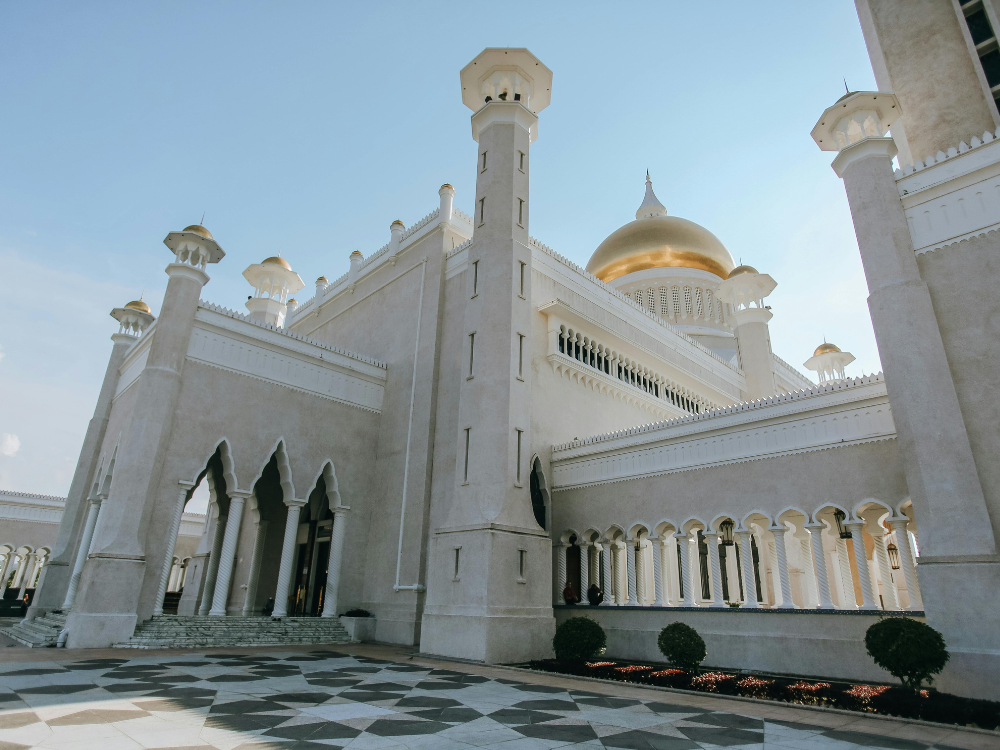 Sultan Omar Ali Saifuddin Mosque with gold dome, white walls, patterned ground, and blue sky.