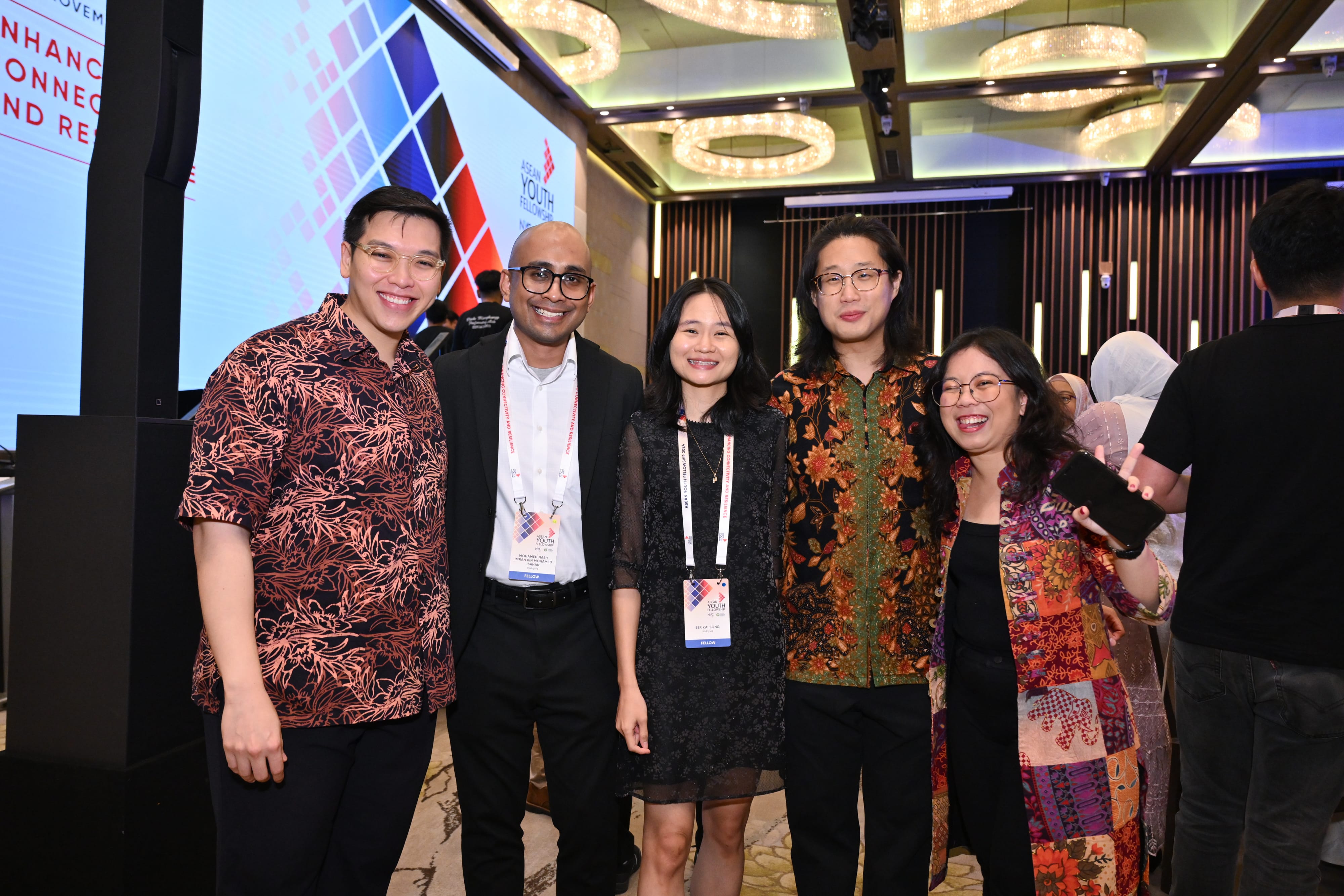 Group of six people posing indoors, some wearing "ASEAN Youth Fellowship" lanyards.