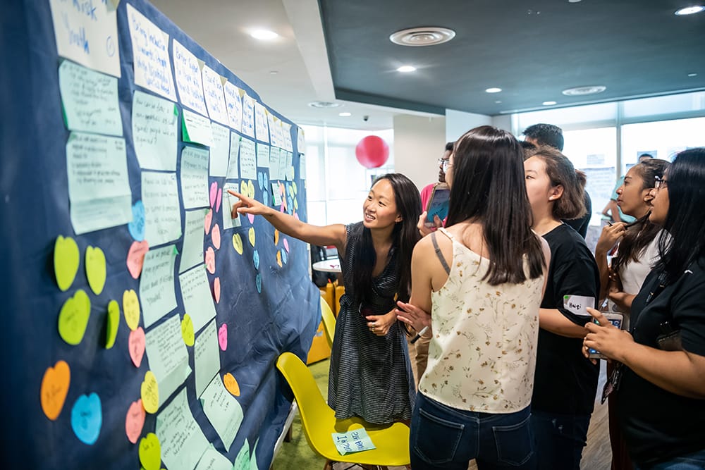 Group of people brainstorming, pointing at sticky notes on a large blue display.