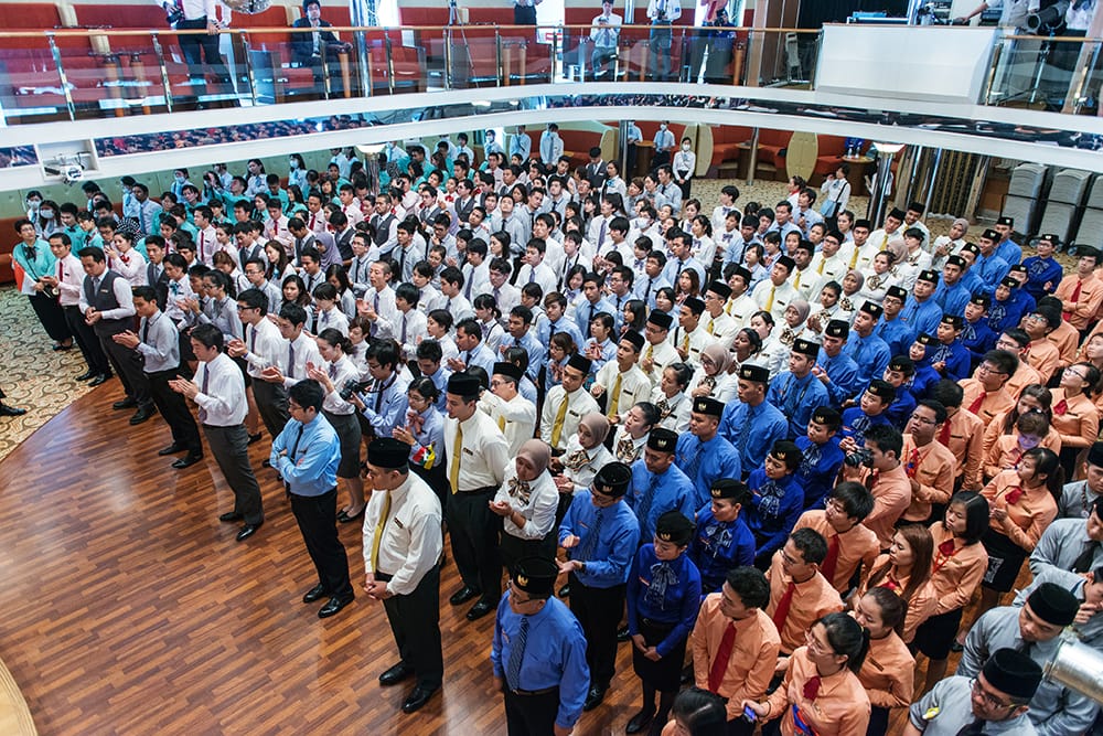 Large group of uniformed students and adults standing in an auditorium.