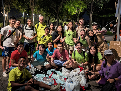 Night cleanup group poses with bags of collected litter and trash pickers in a park setting