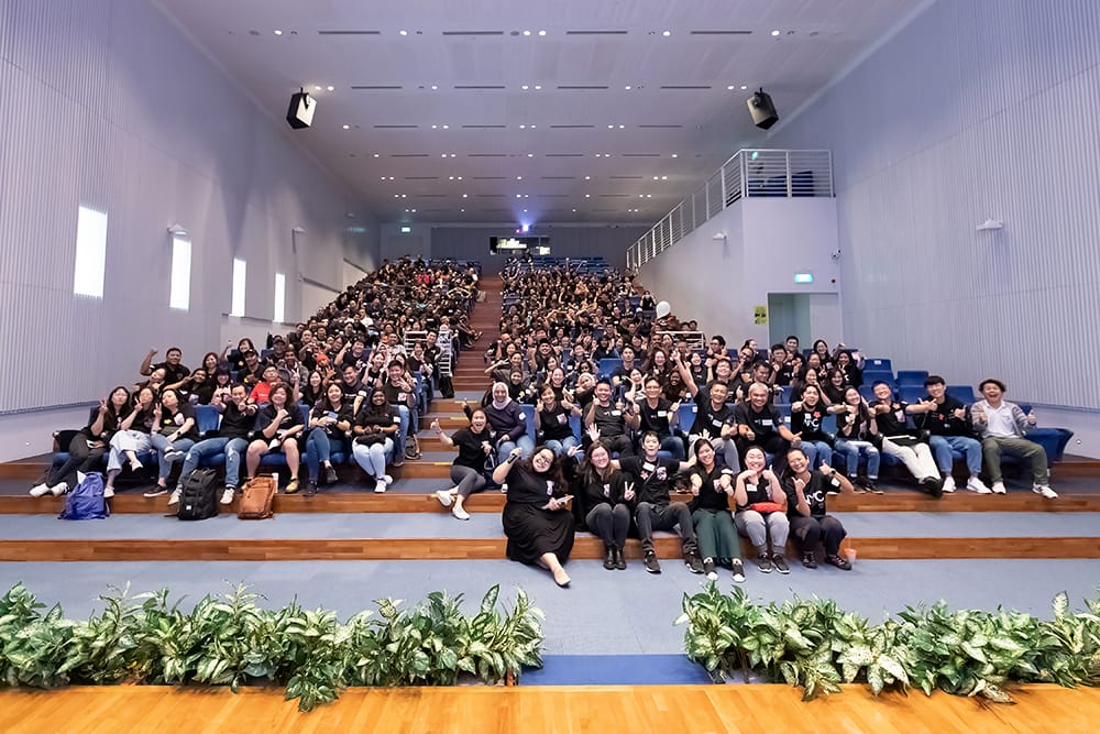 Group photo of diverse individuals sitting in an auditorium, making peace and thumbs-up gestures